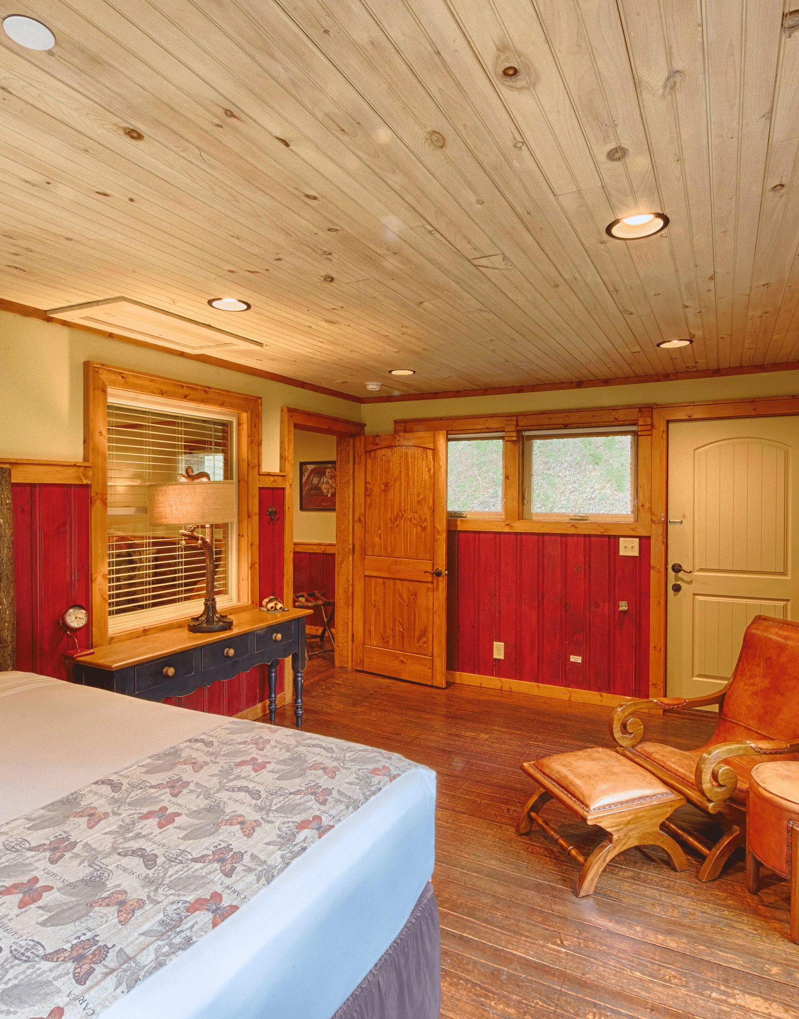 a bedroom with an armchair in the corner and a double bed along with an open door in the far end of the room - Historic Tapoco Lodge