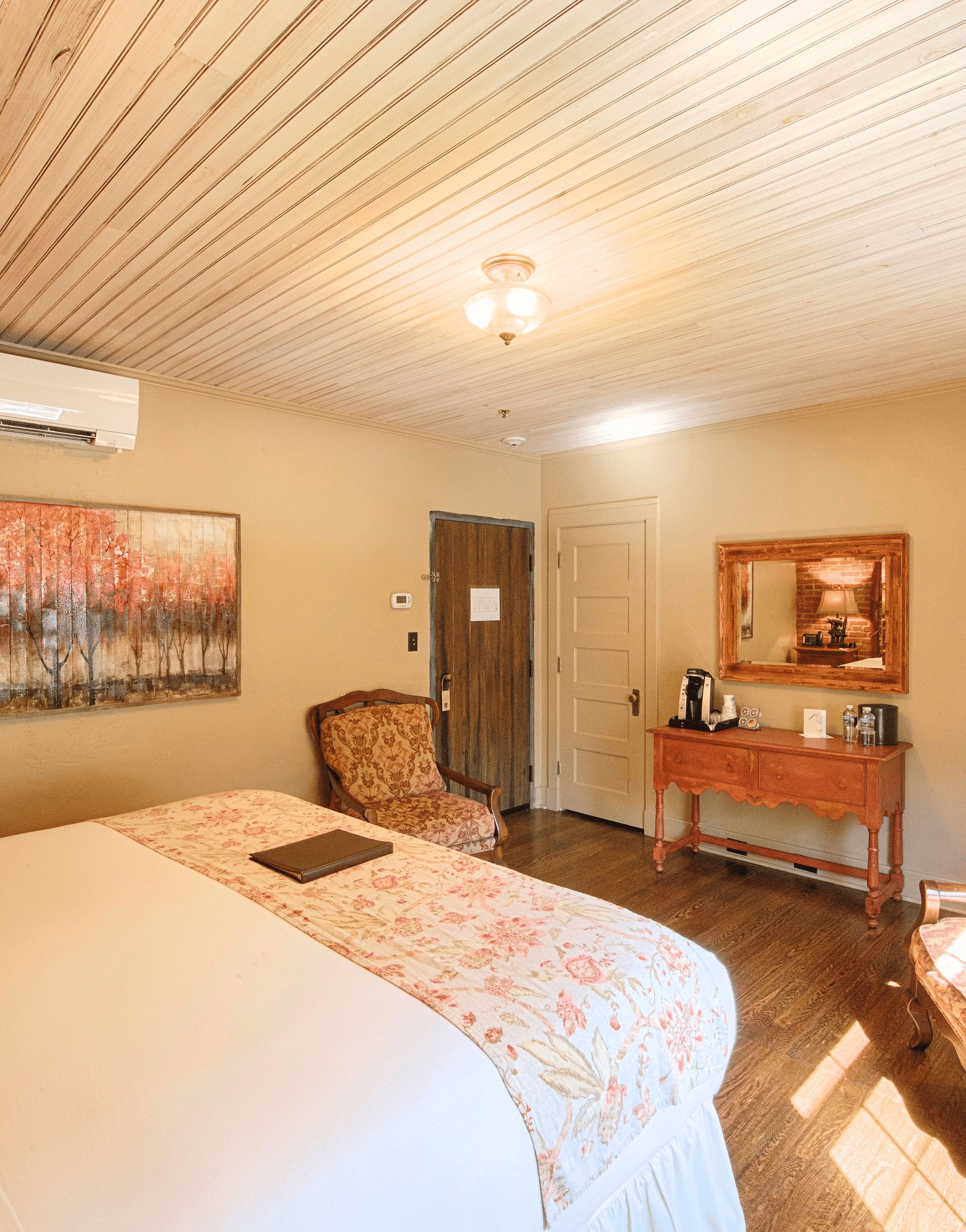 corner view image of a bedroom with two armchairs facing towards each other in front of the bed along with a wall mounted air-conditioner - Historic Tapoco Lodge