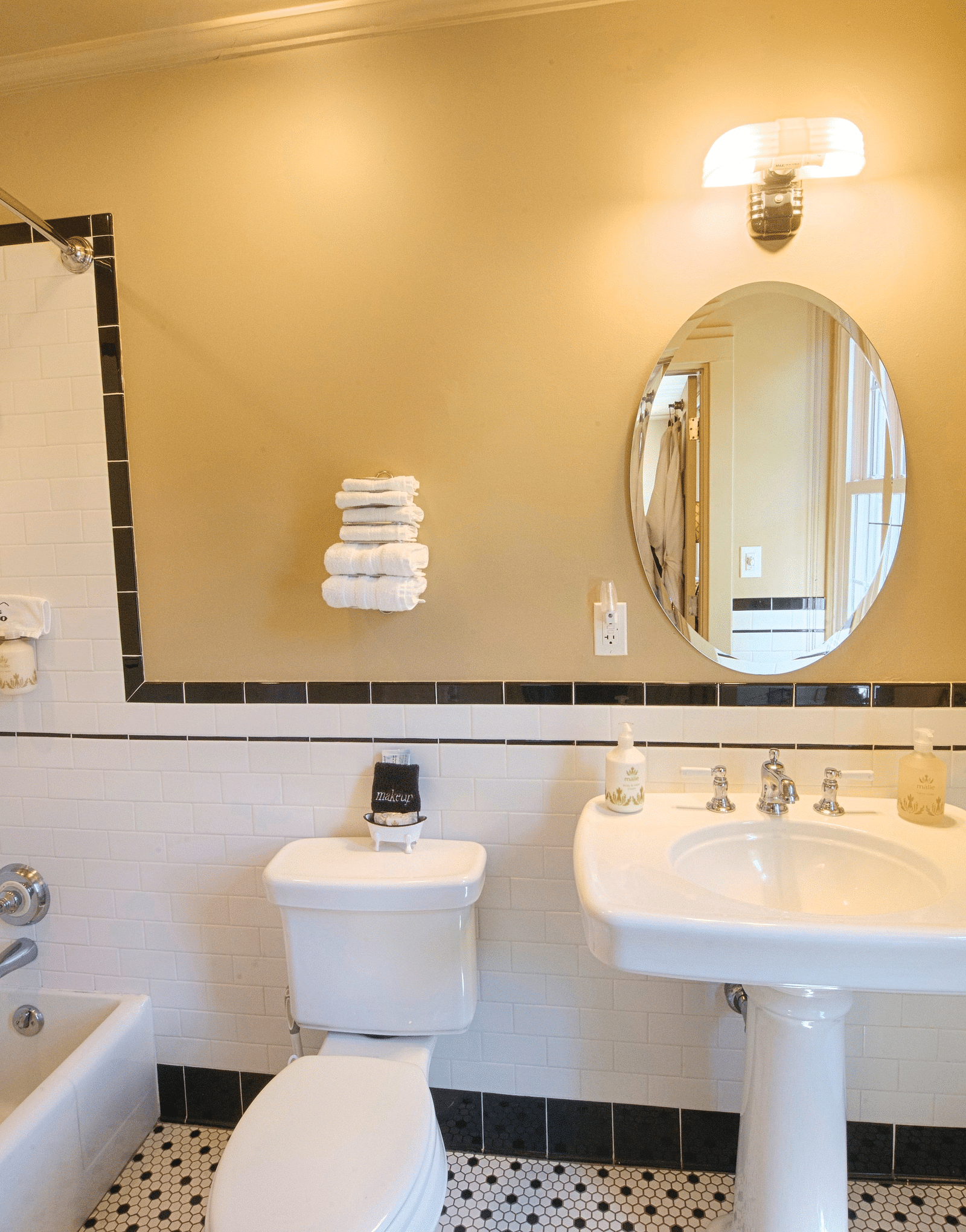 a bathroom highlighting a wash basin with an oval shaped mirror along with a commode and a bathtub besides it - Historic Tapoco Lodge