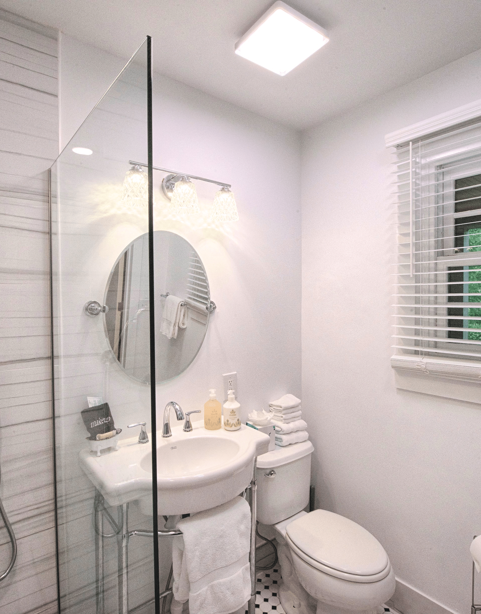 a bathroom with a wash basin along with a wall mounted circular mirror and a commode beside it with a small window for ventilation - Historic Tapoco Lodge