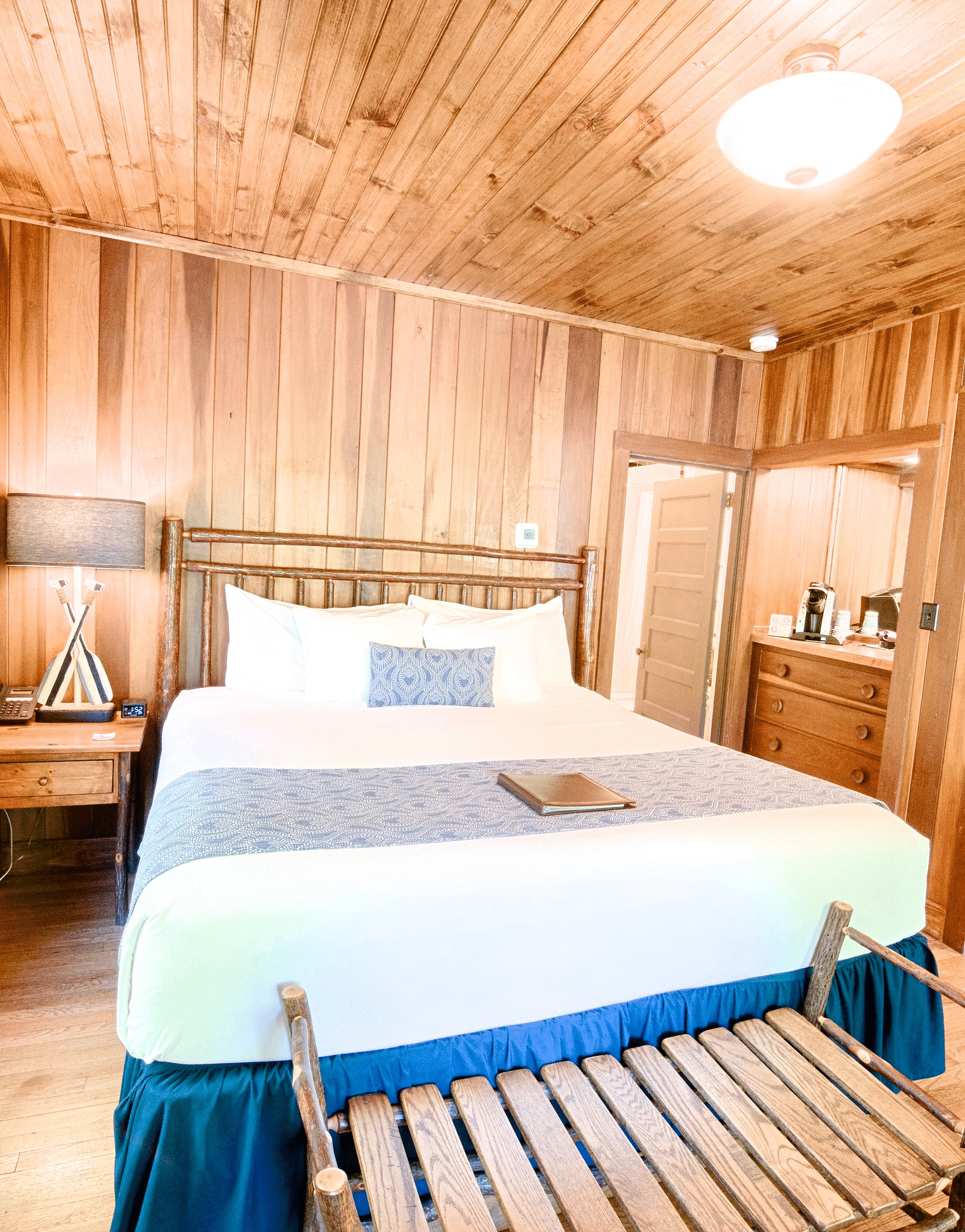 a bedroom featuring a a plush double bed with a window besides it and a small sitting bench in front of the bed - Historic Tapoco Lodge