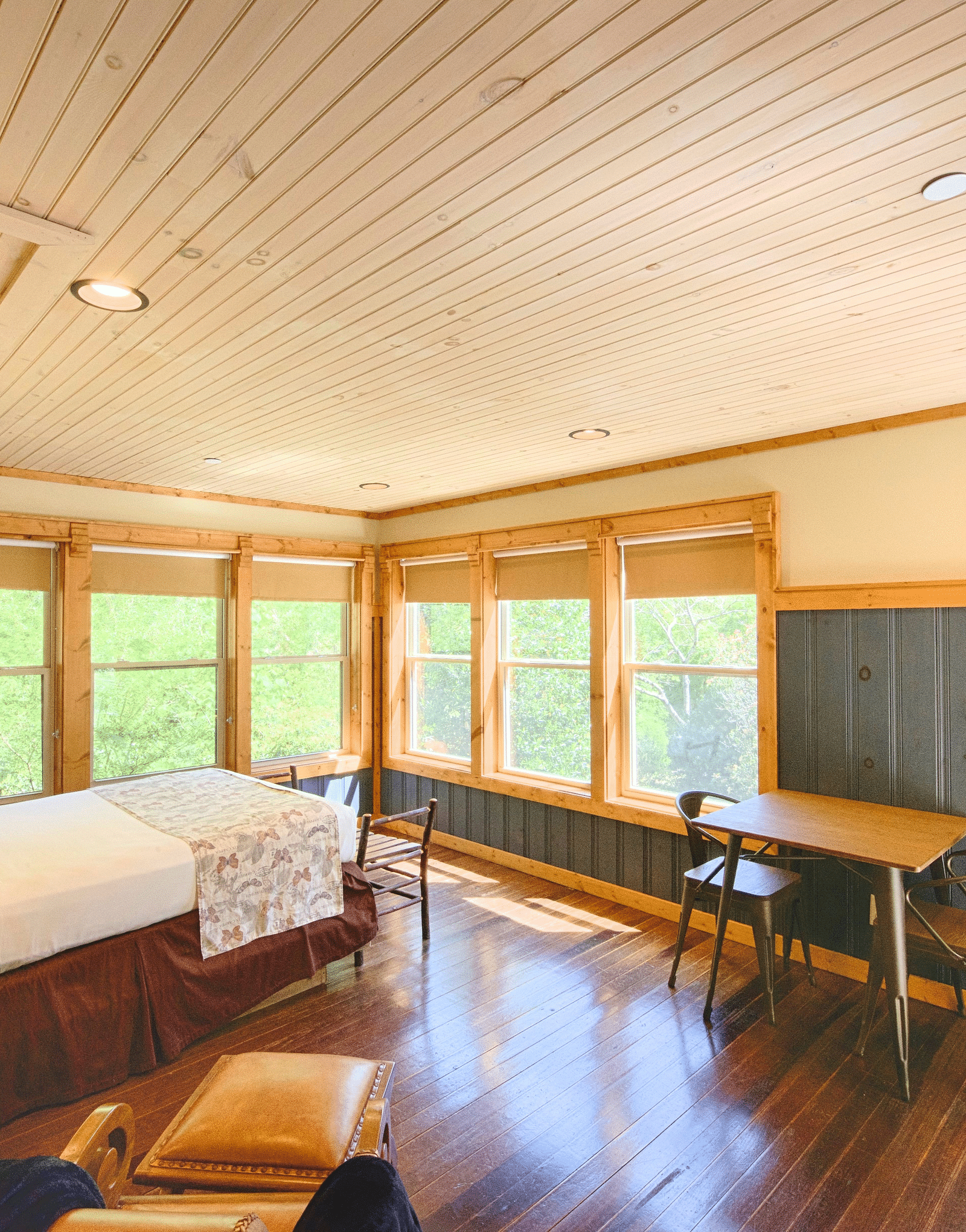 a bedroom with a double bed overlooking the scenic views of the forest form the windows with wooden flooring and colorful interiors of the room - Historic Tapoco Lodge