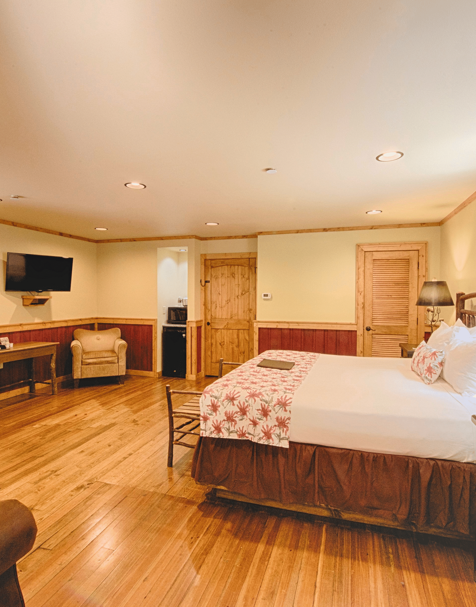 a plush double bed with a lamp placed on a bed side table along with a wall mounted television in the corner - Historic Tapoco Lodge