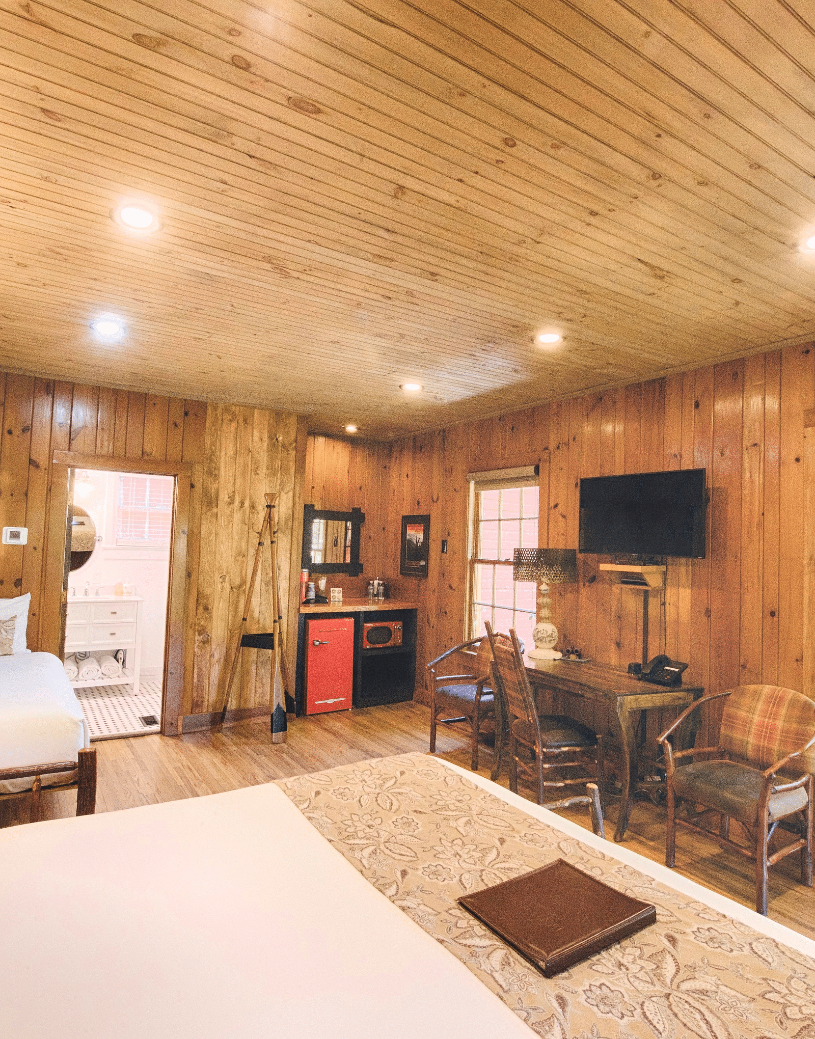 a bedroom overlooking a double bed with a file kept on it facing towards a window with lush green views outside - Historic Tapoco Lodge