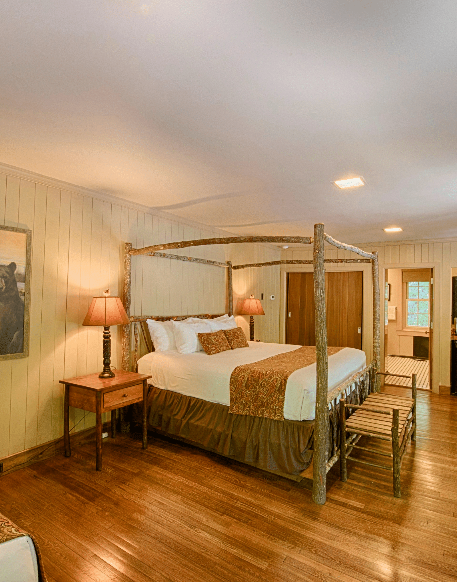 a cozy bedroom with a wall mounted art piece besides a double bed and a dressing table at the far end of the room - Historic Tapoco Lodge