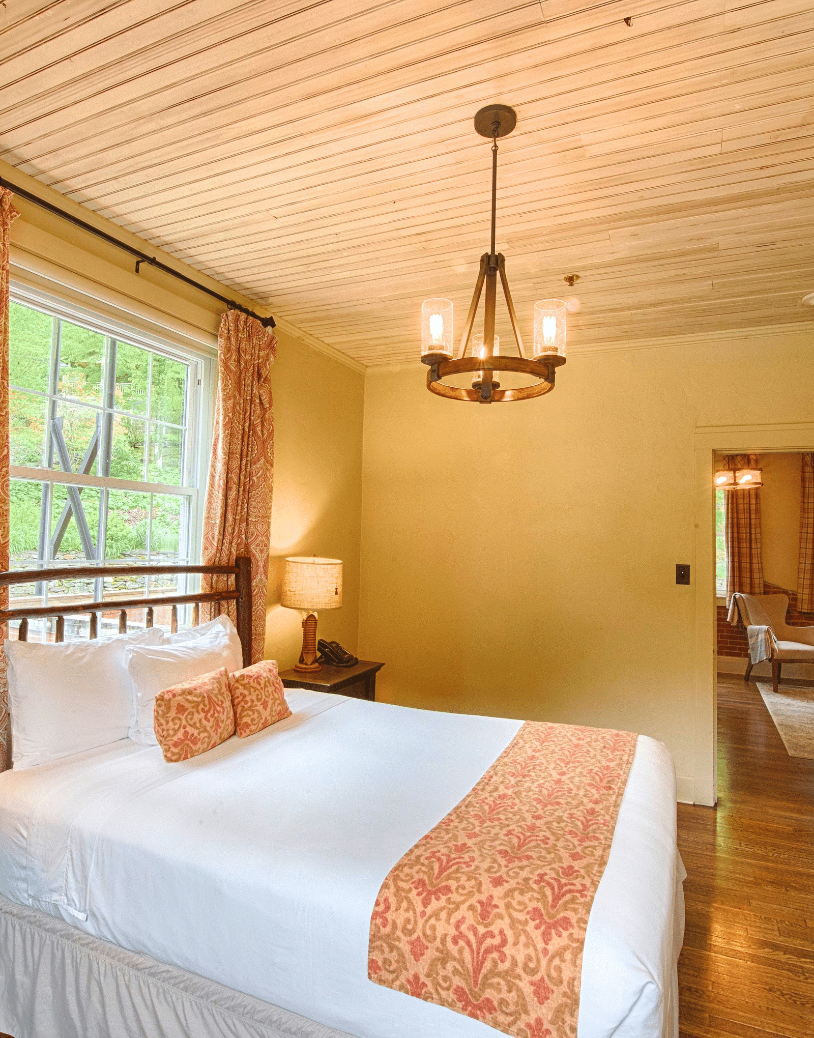 side view image of a double bed right under the chandelier with a window behind the bed - Historic Tapoco Lodge