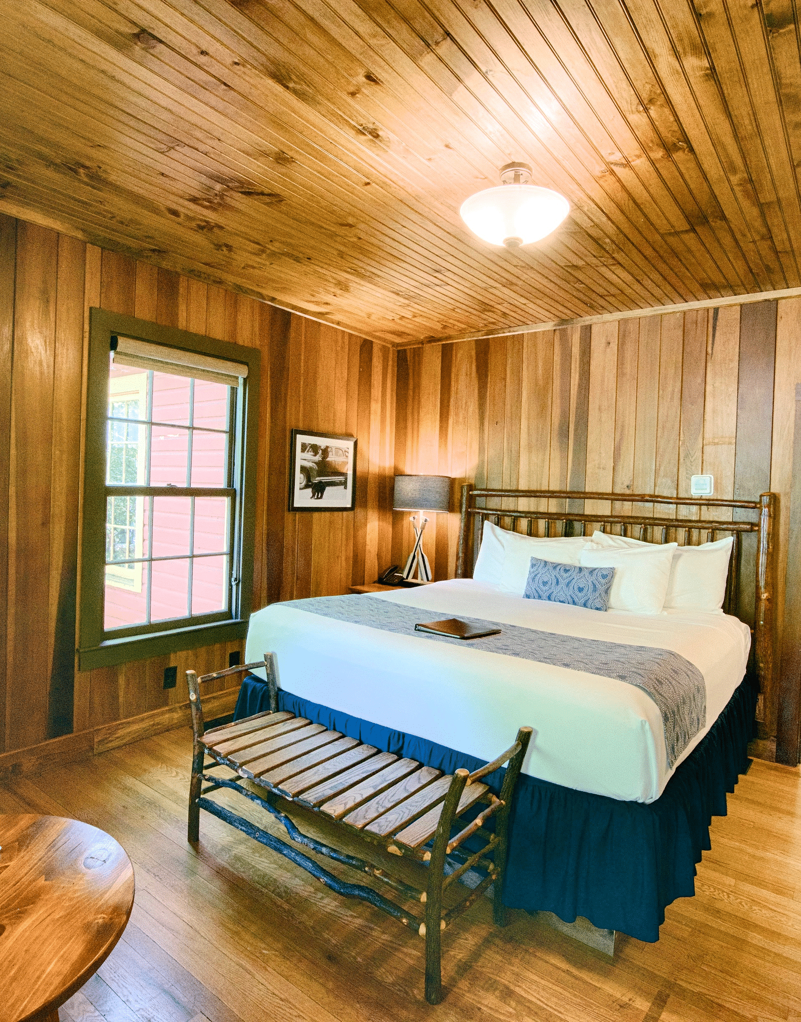 a wide angle shot of a bedroom with a modern looking table lamp kept on the round wooden coffee table - Historic Tapoco Lodge
