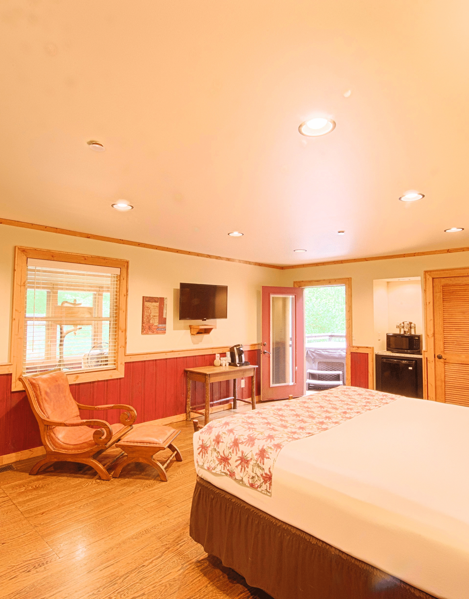 a double bed placed in front of a cushioned armchair that is besides a door frame leading to the other bedroom - Historic Tapoco Lodge