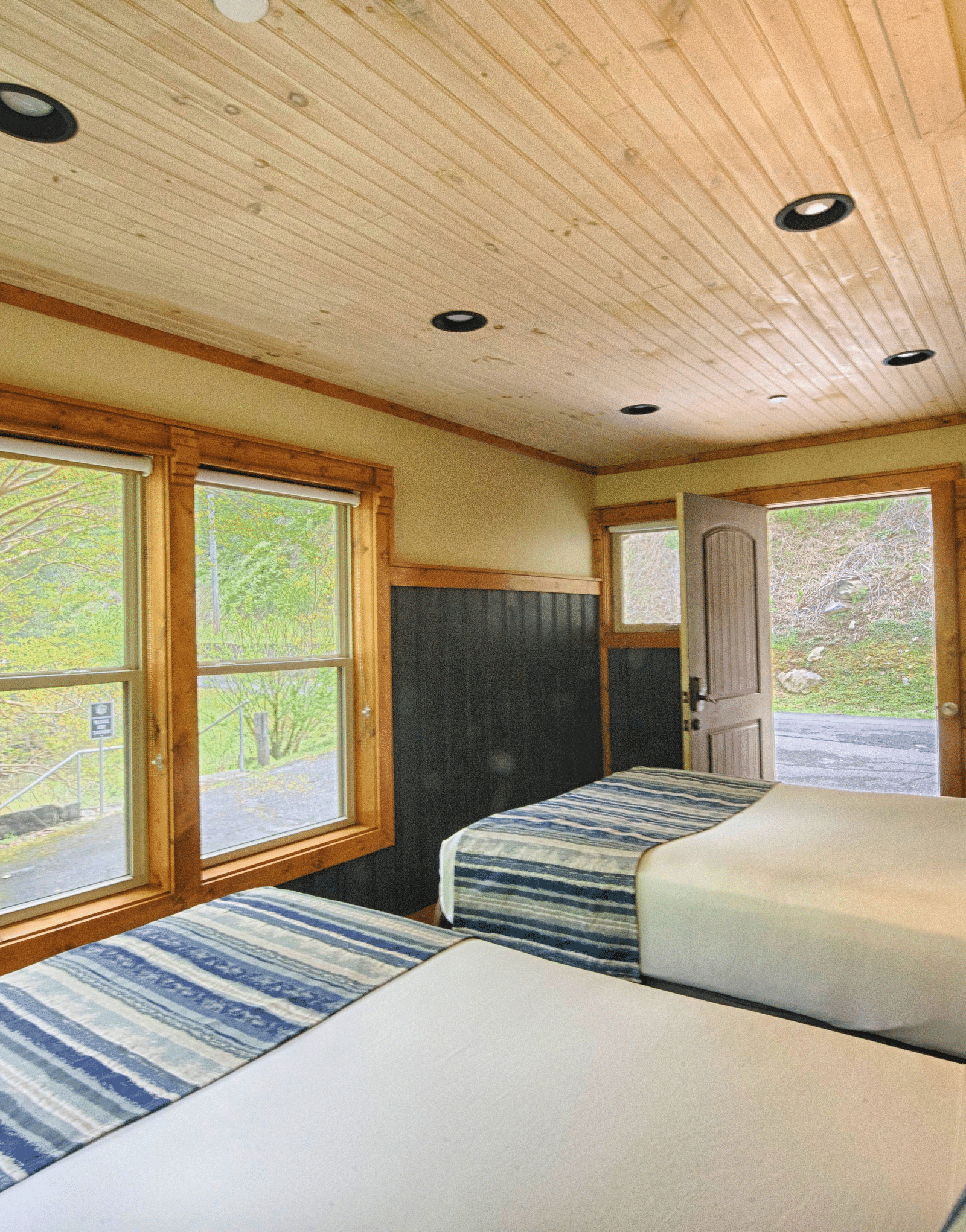 two double beds facing towards the huge windows with lush green forest views and a door opening to the exterior - Historic Tapoco Lodge