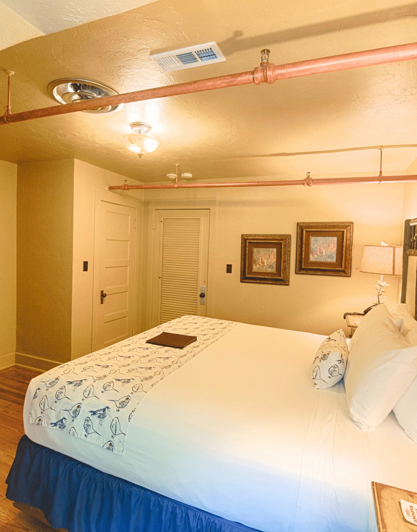 corner view image of the bedroom with two wide framed photos wall mounted in the corner and a wooden drawer in front of the bed - Historic Tapoco Lodge