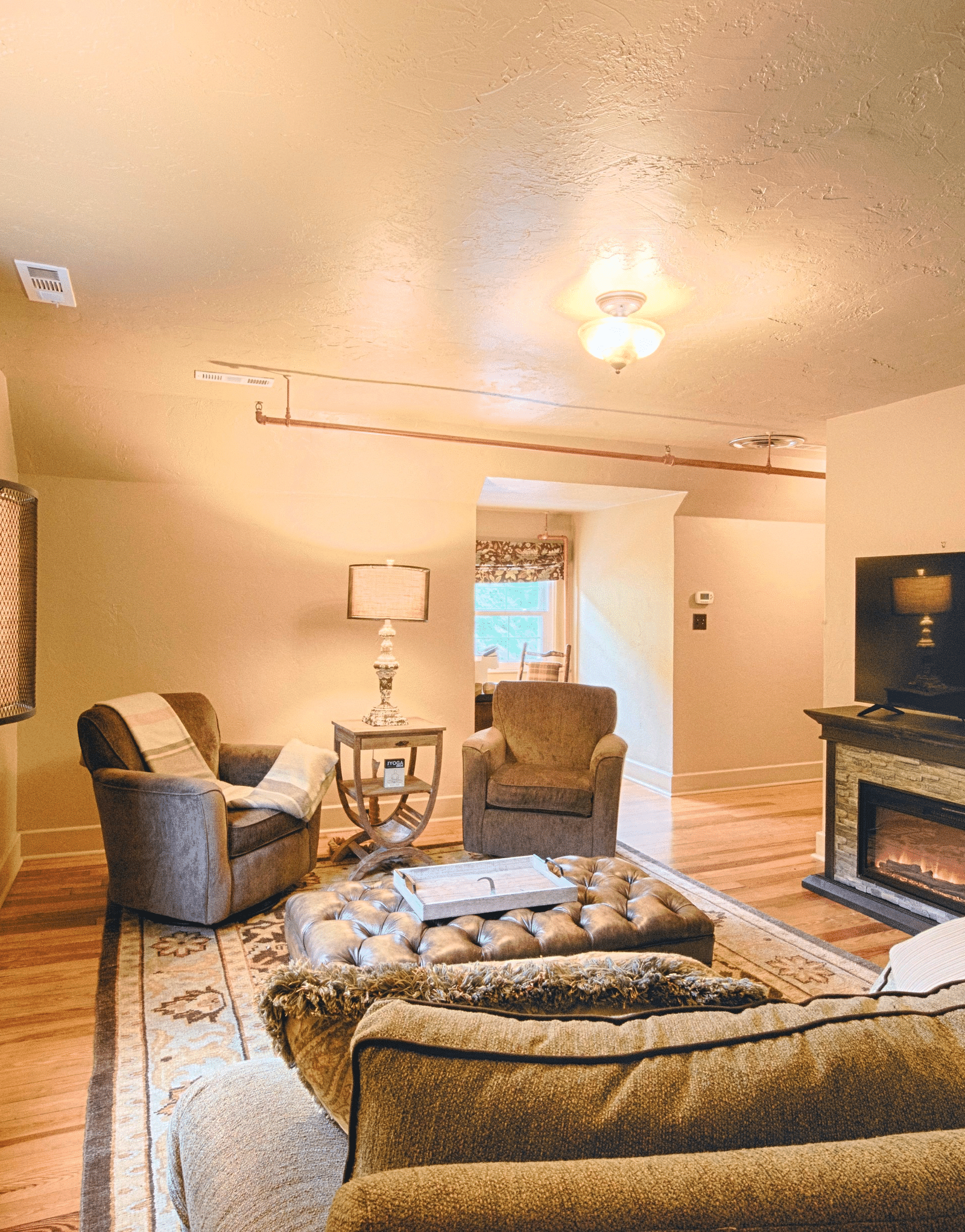 corner view image of the living room featuring a cozy seating area with an electric fire place and a flat screen television - Historic Tapoco Lodge