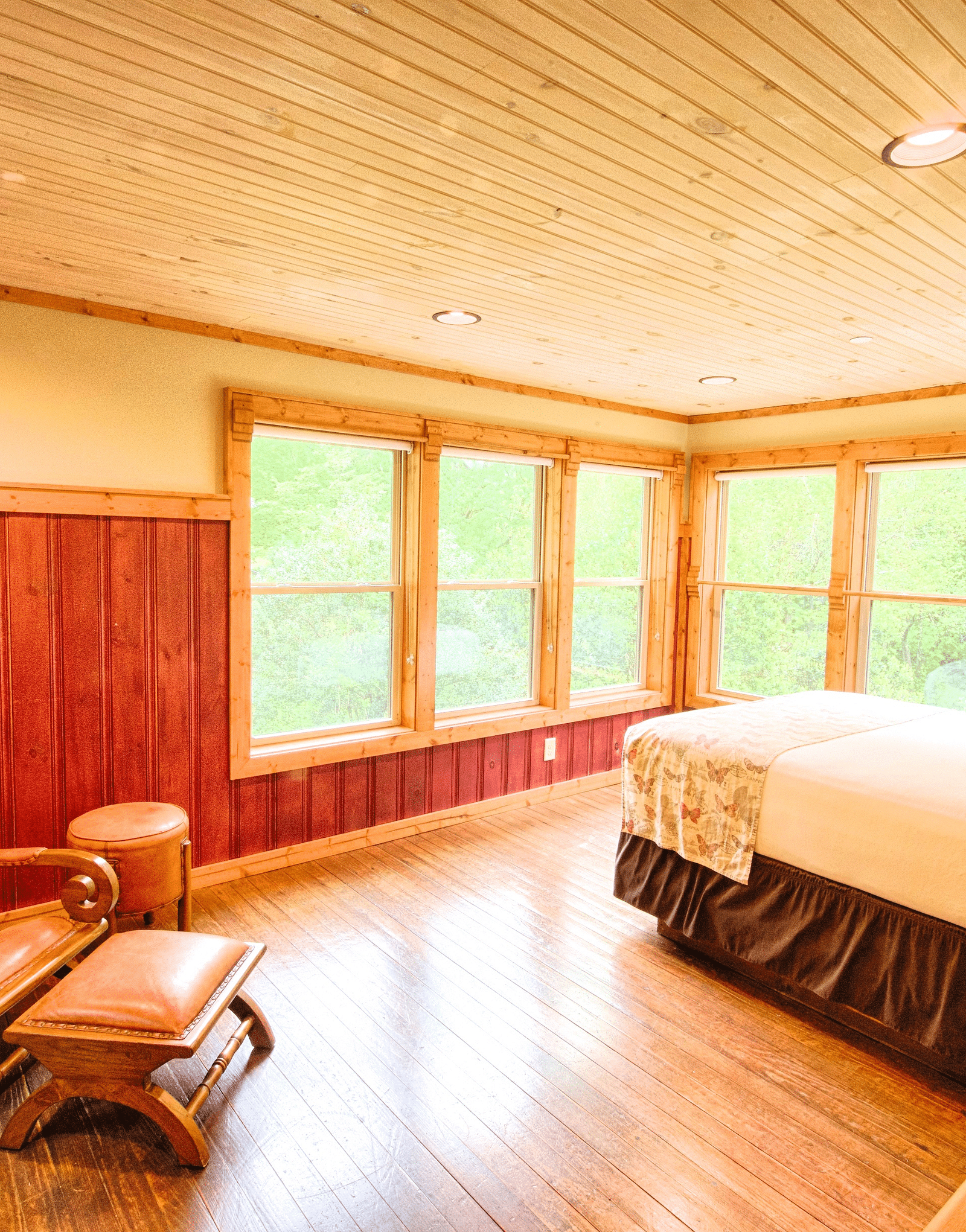 corner view image of a vibrant bedroom with an armchair and a bed overlooking the beautiful green forest - Historic Tapoco Lodge