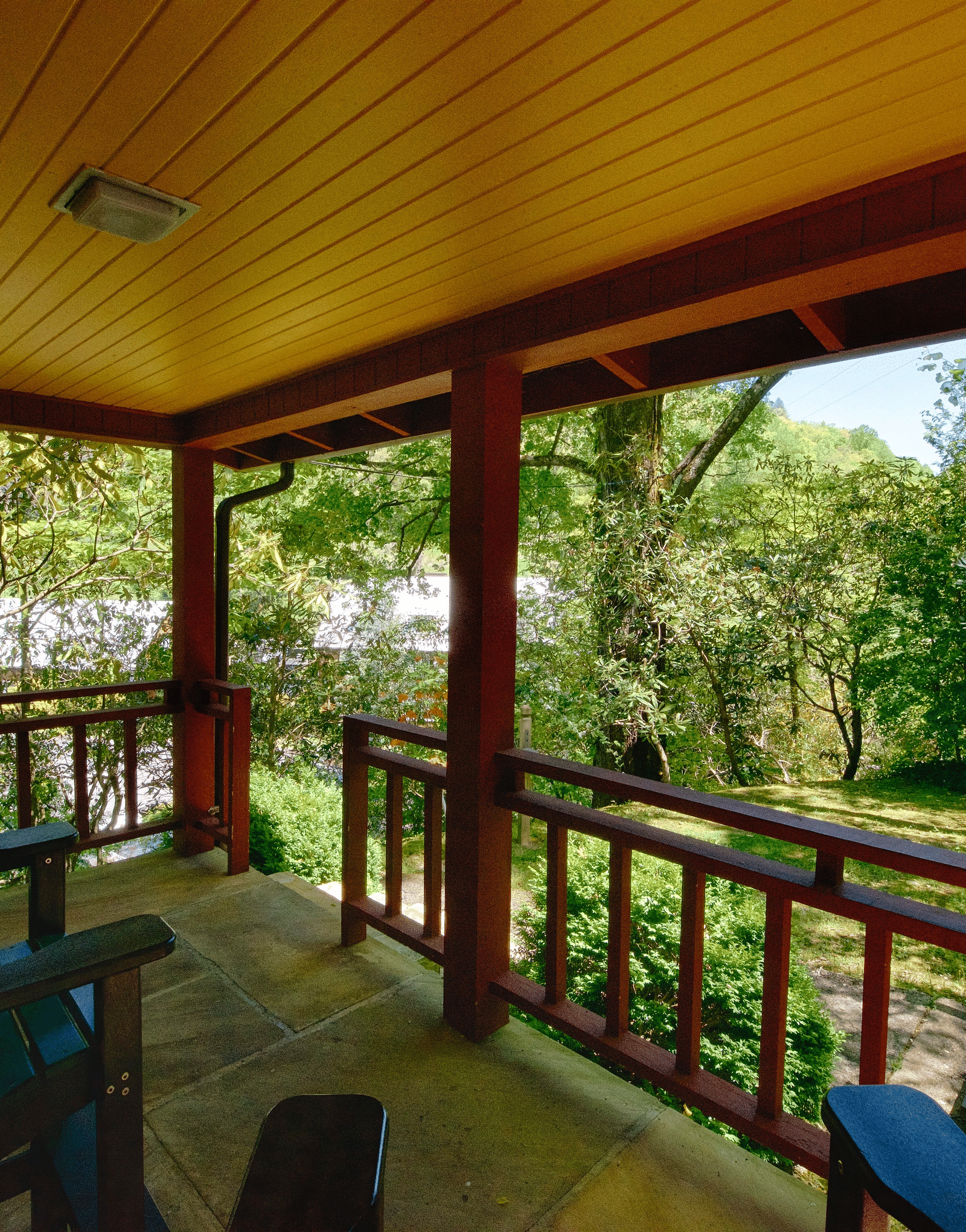 a beautiful wooden porch with chairs kept on it facing towards the green forests - Historic Tapoco Lodge