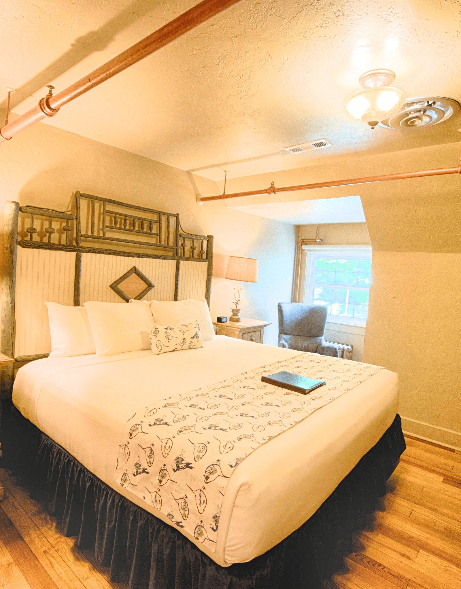 a comfortable double bed with a huge head board behind it in a warmly illuminated room - Historic Tapoco Lodge