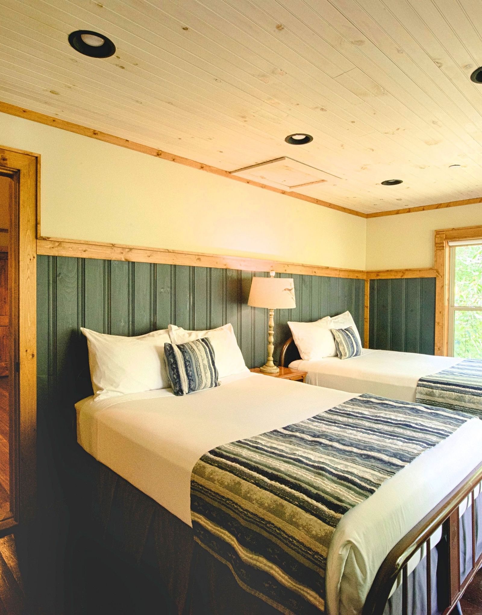 a room with ample natural light featuring two single beds with an open door frame besides them - Historic Tapoco Lodge