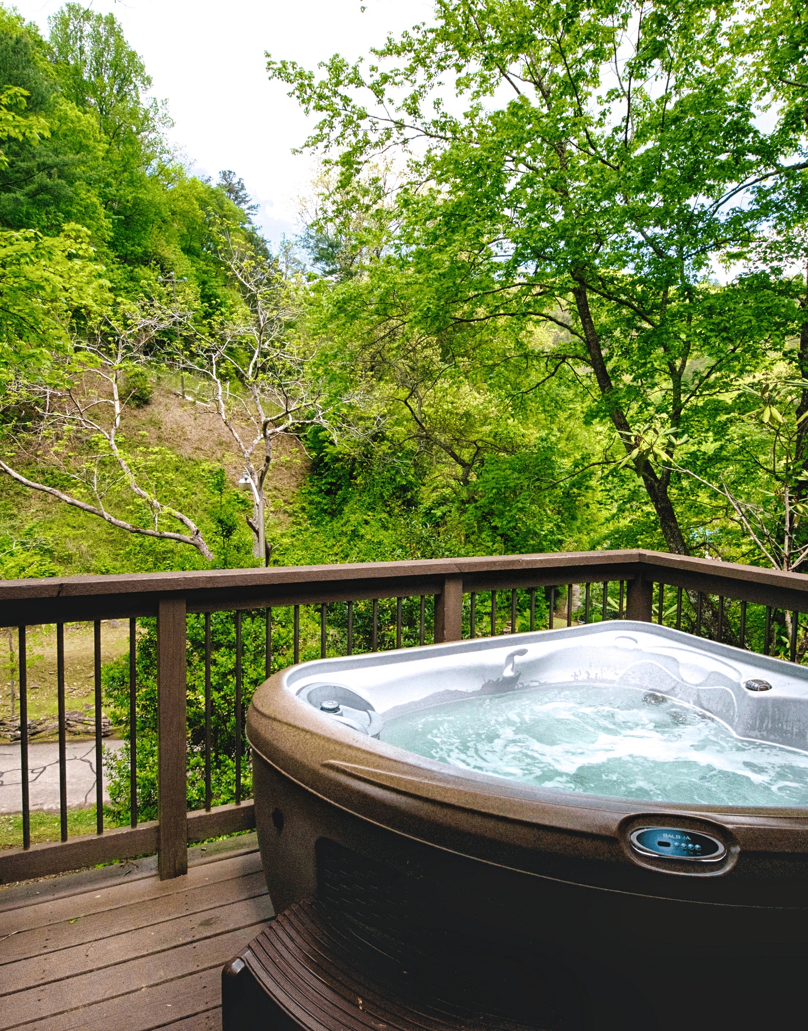 a wooden porch with hand railings along with a Jacuzzi tub overlooking the beautiful surrounding forest views - Historic Tapoco Lodge