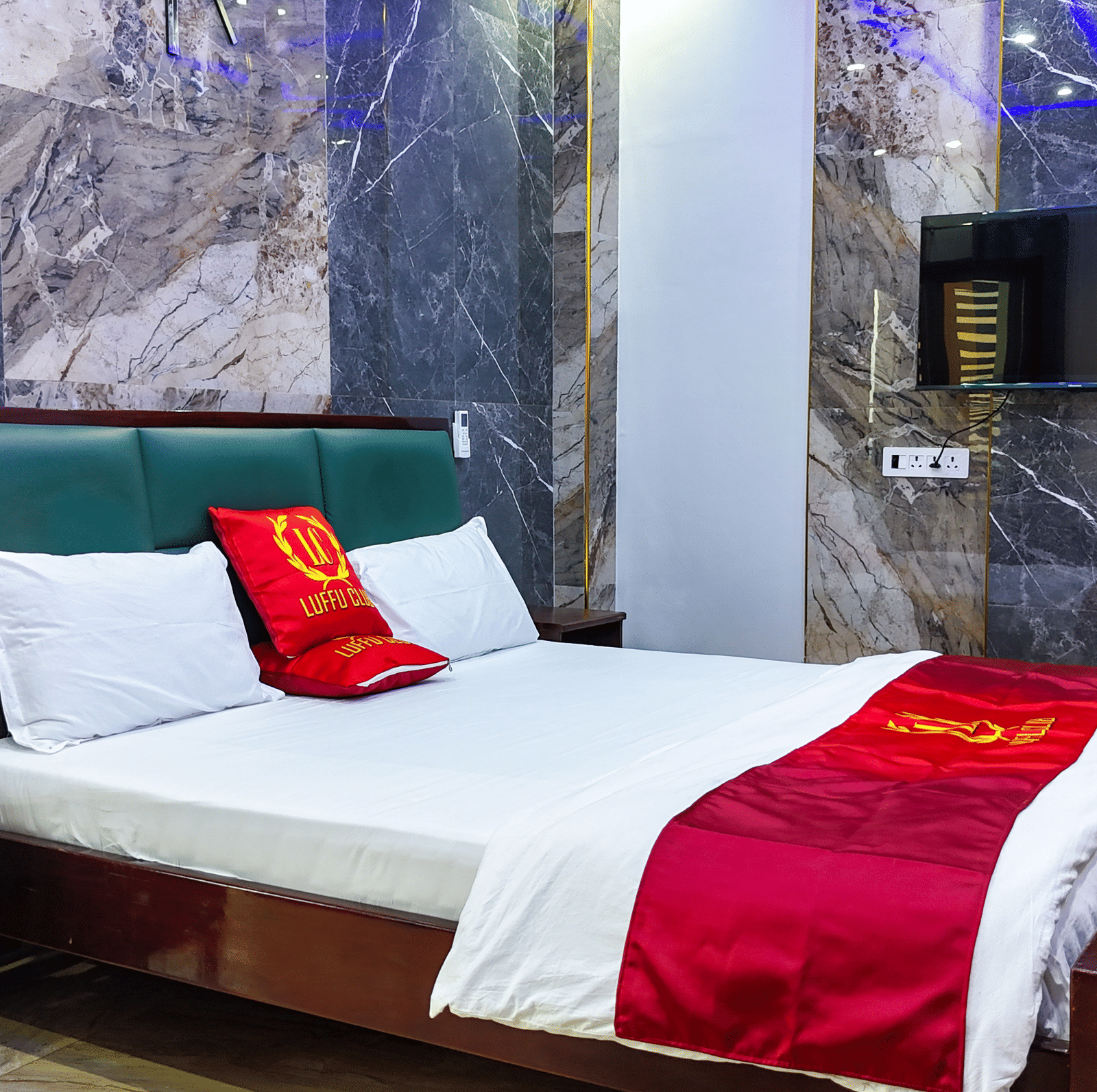Room with a bed, red accents sheets, and marble-style wall panelling - Luffu Club