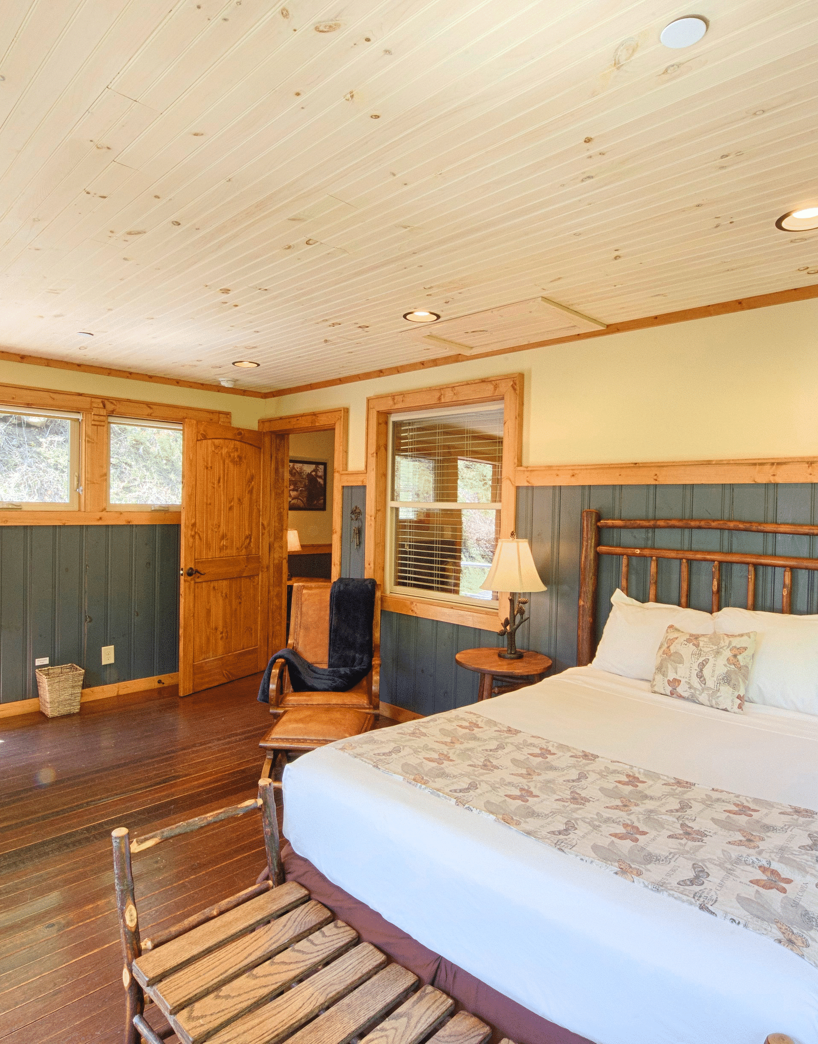 front view image of a bedroom with vibrant interiors and wooden flooring featuring a double bed with a vintage tall lamp besides it -Historic Tapoco Lodge