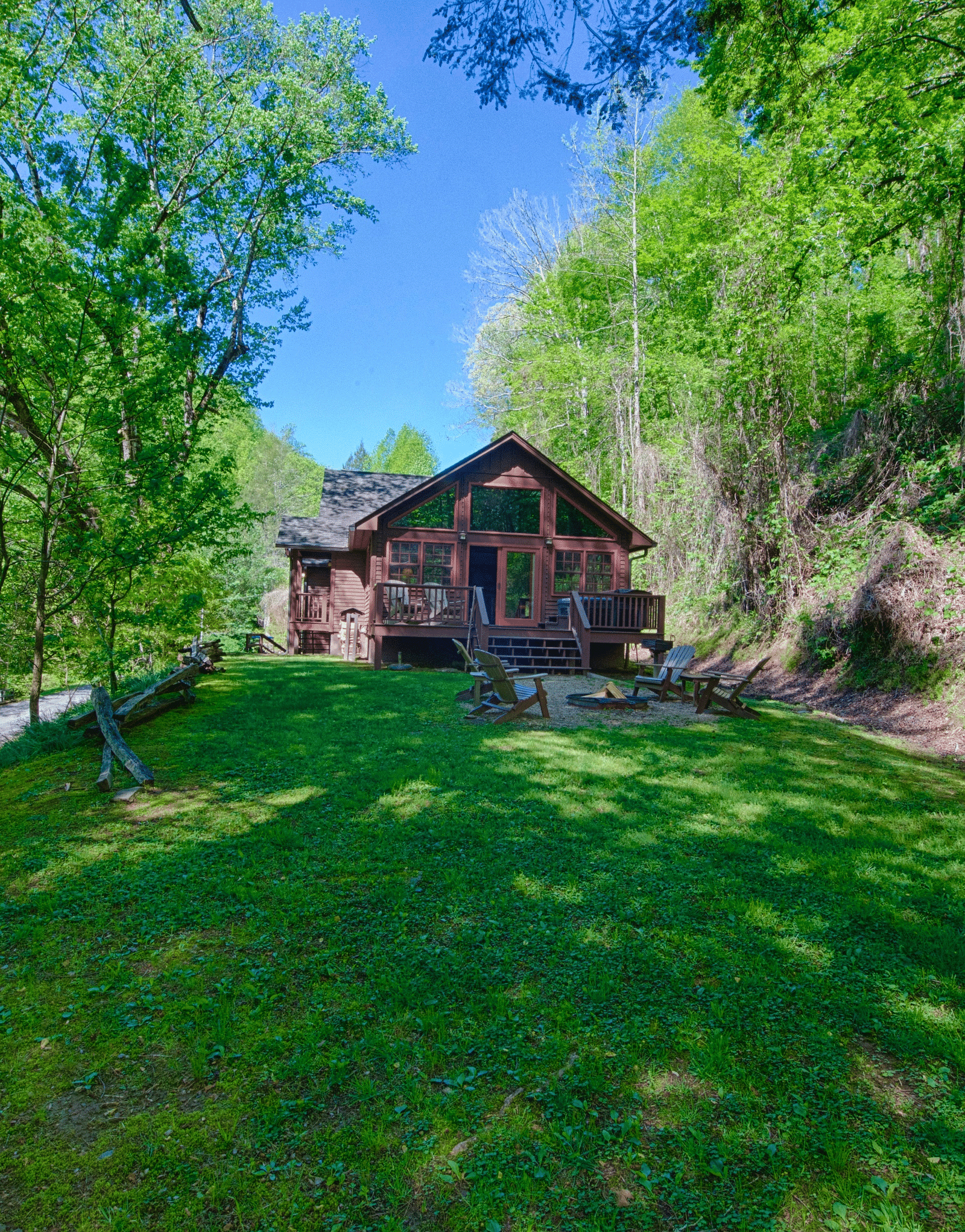a wide angle shot of a wooden cabin surrounded by tall green trees overlooking an expansive lawn - Historic Tapoco Lodge