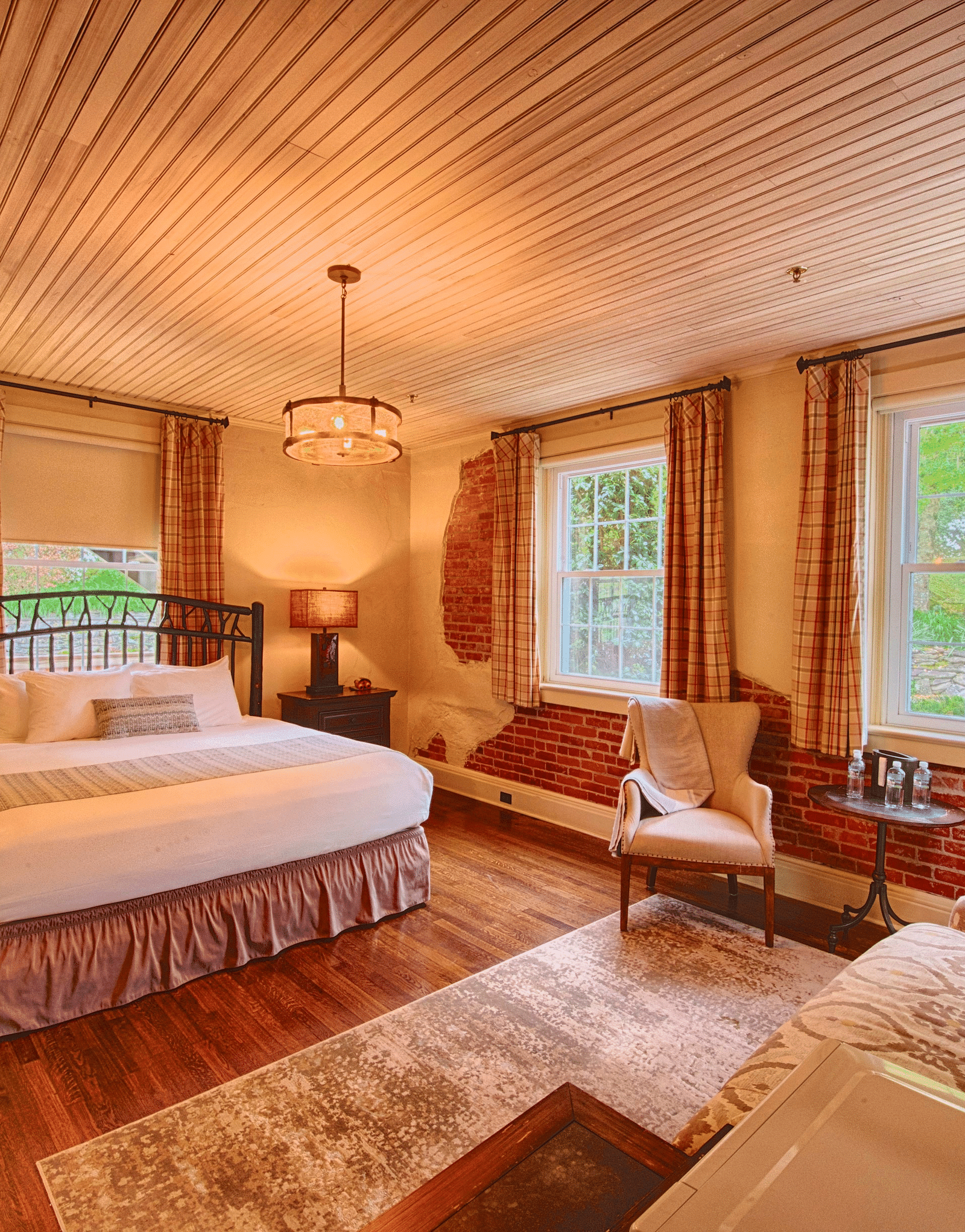 a room with ample natural lighting coming from the huge windows in the room with plush arm chairsa brightly lit bathroom featuring a door opening to the bedroom overlooking the double bed - Historic Tapoco Lodge