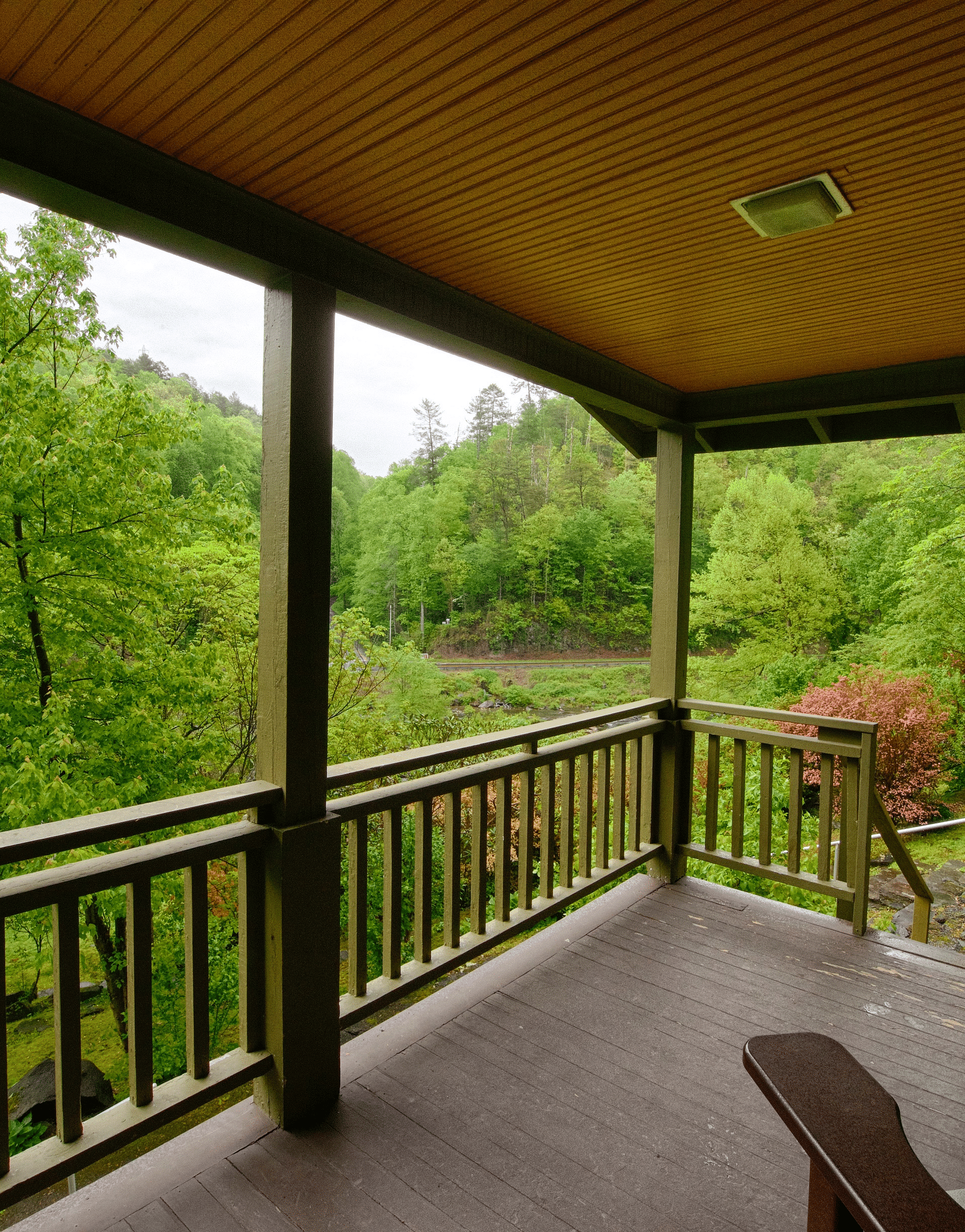 side view of a porch with wooden chairs placed on it overlooking the lush green scenic views - Historic Tapoco Lodge