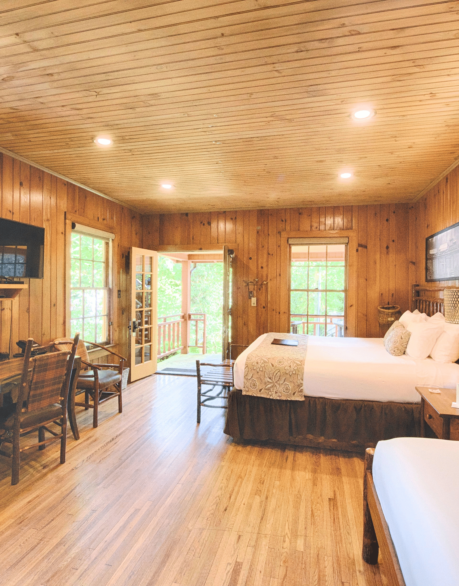 a room with a leather arm chair right in front of the window with a lamp kept on the TV table - Historic Tapoco Lodge