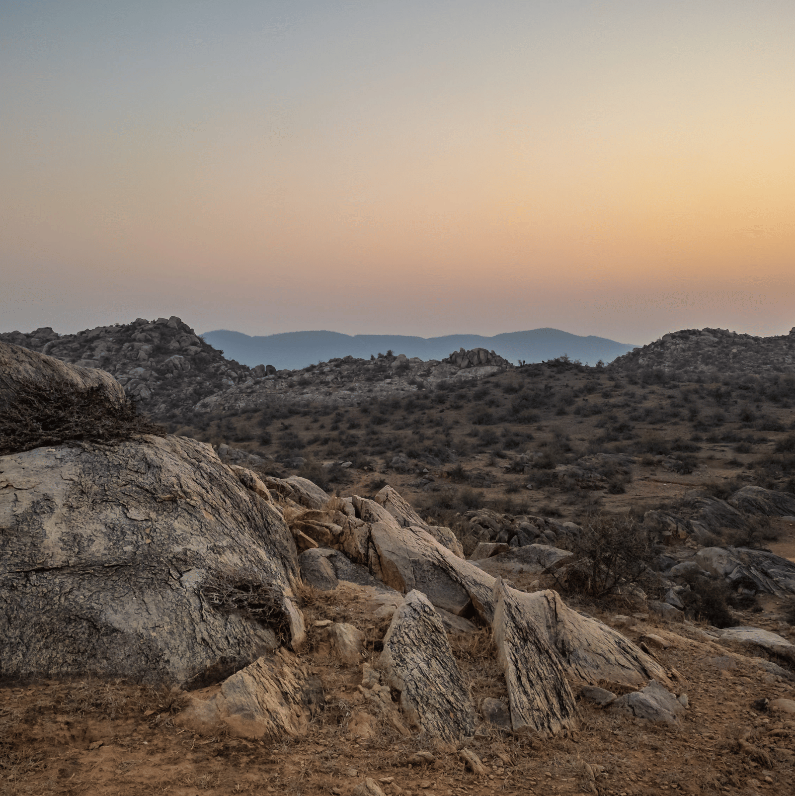Overcast sunset view of a valley with rocky hills, golden light on the horizon.