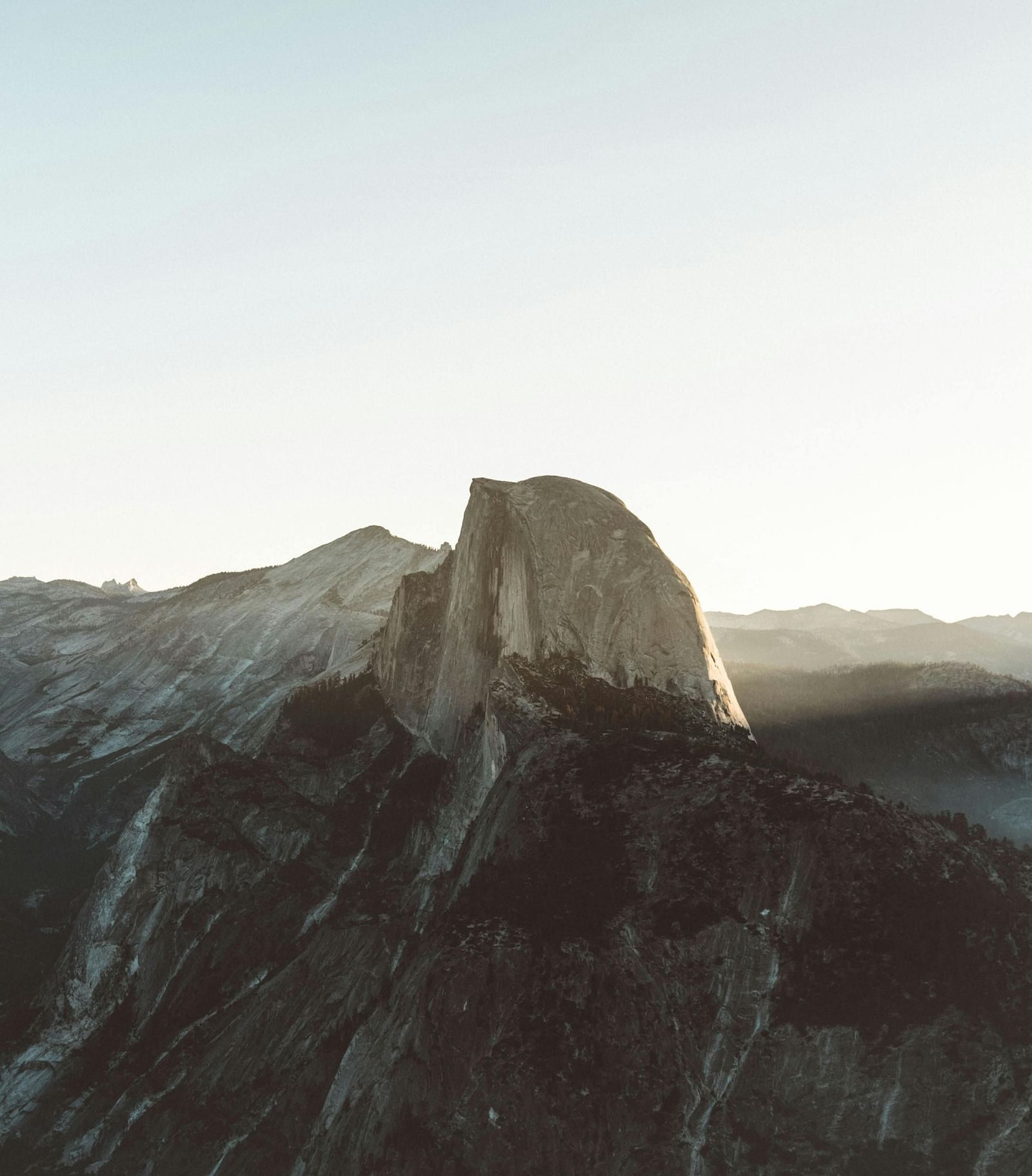 A breathtaking view of Glacier Point in Yosemite with a towering peak bathed in soft, golden sunlight, surrounded by rugged mountain ranges.