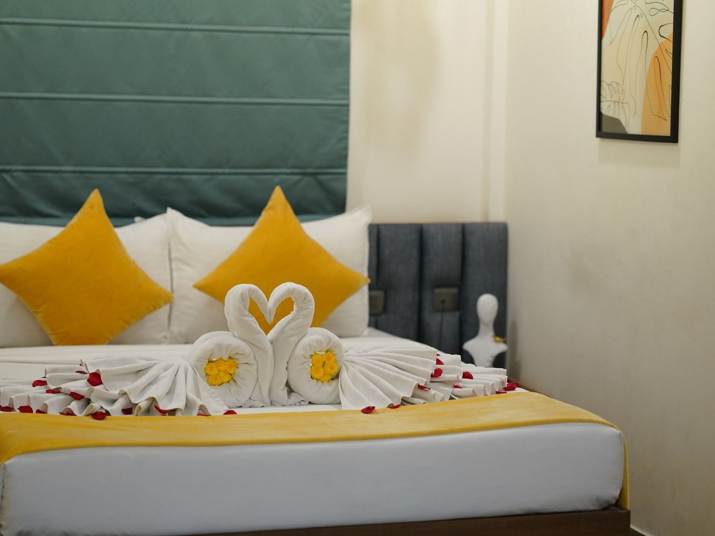 A room with a neatly made double bed adorned with yellow and towels shaped into swans, scattered with rose petals for a welcoming touch at Kyzen Smart Stays.