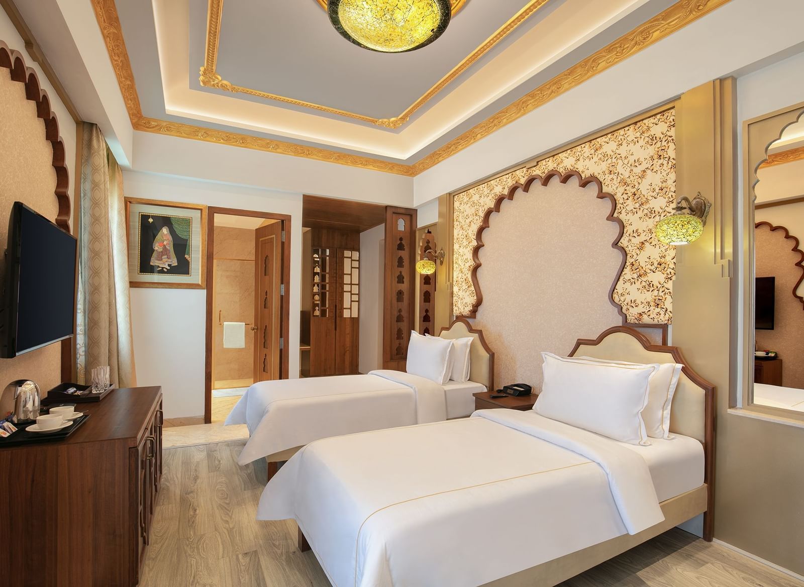 A room with twin beds, ornate golden accents, and a decorative wall panel – Kaldan Samudra, a luxurious beach resort in ECR