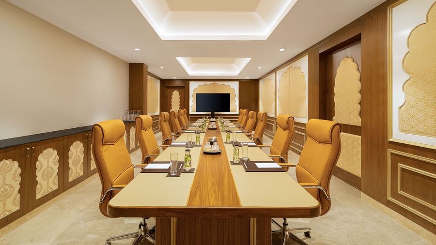 A boardroom in Mahabalipuram with a long table, cosy orange chairs, and rajasthani decor - Kaldan Samudhra Palace