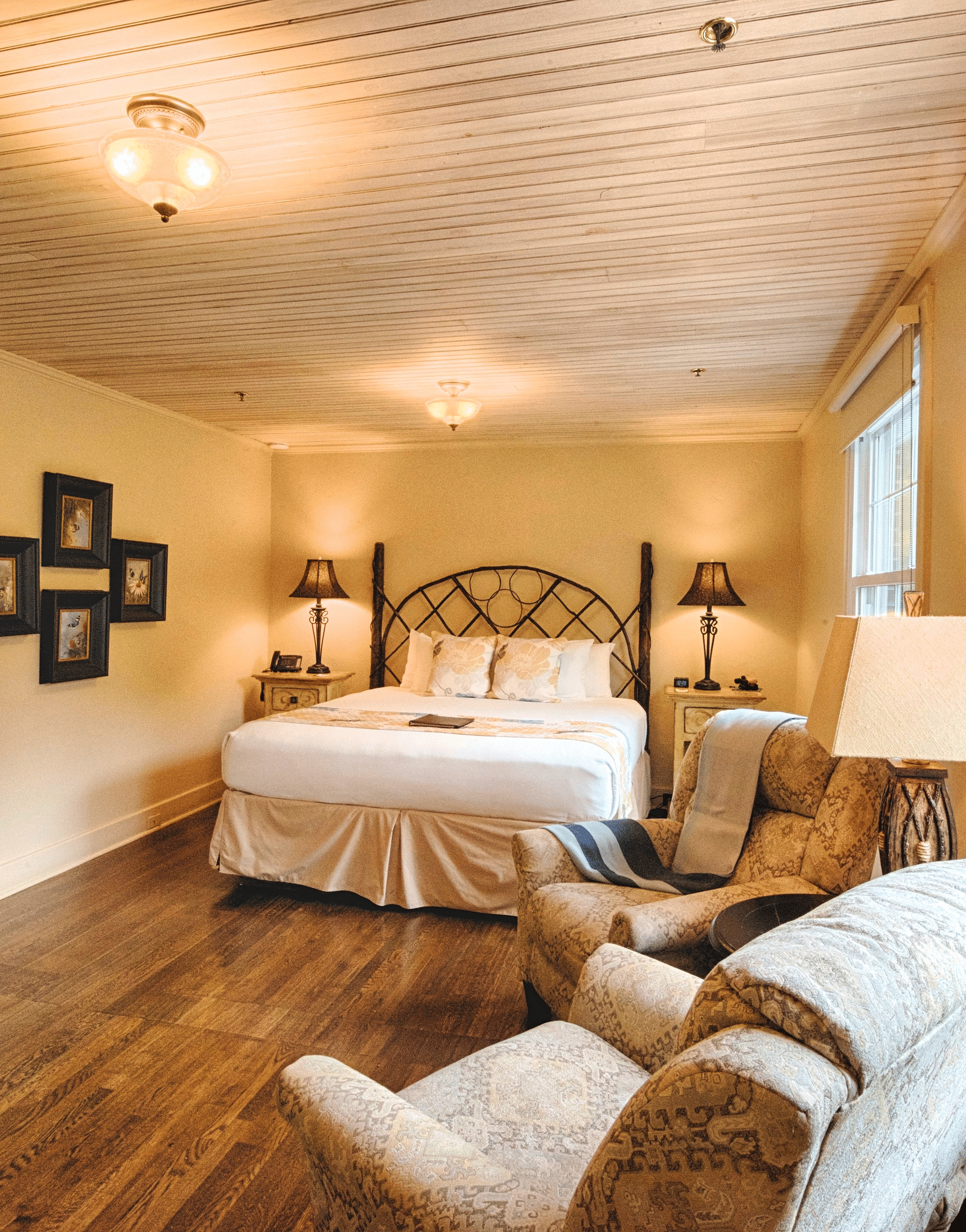 a room with wooden flooring and cream colored walls featuring a double bed in the middle of the room along with a seating area - Historic Tapoco Lodge