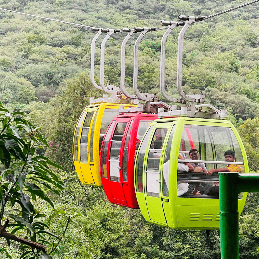 Red, yellow, and green cable cars suspended above forested hills on the Karni Mata Ropeway