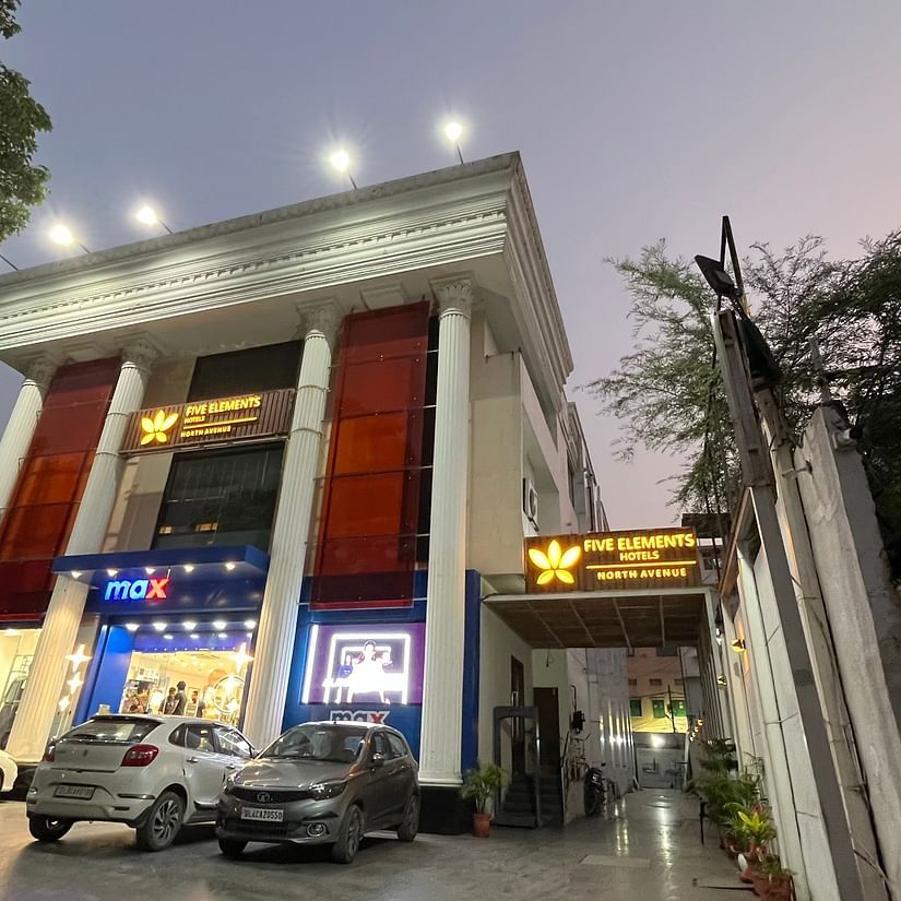 An image of a well lit facade of Five Elements Hotels North Avenue, Delhi which is surrounded by commercial buildings and trees