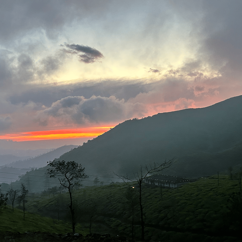 Orange sunset partially hidden by soft, rolling clouds at Ibex Resorts, the best resort in Valparai.