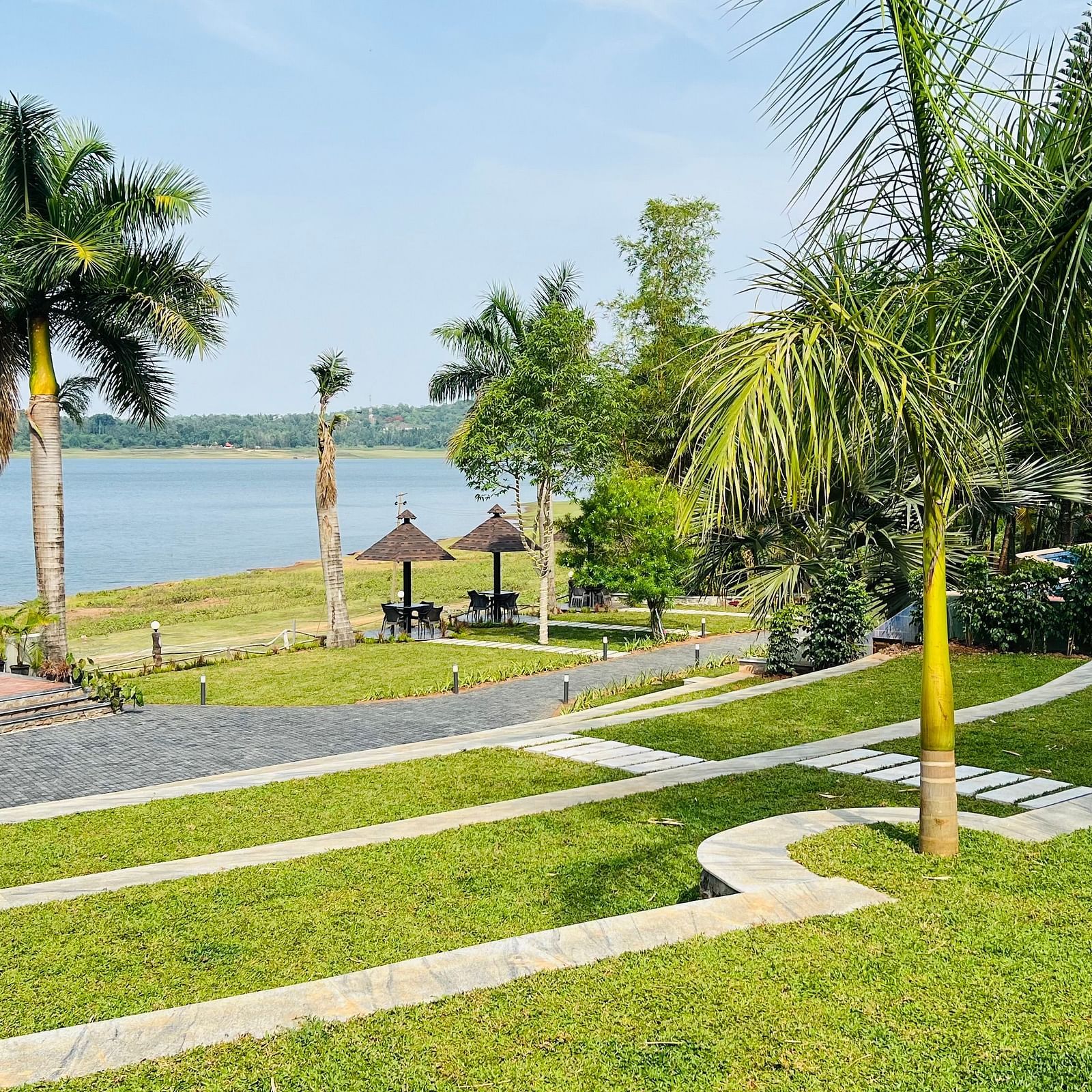 Scenic stepping stone path leading to backwaters at Coorg Jungle Camp Resort, surrounded by lush lawns and palm trees