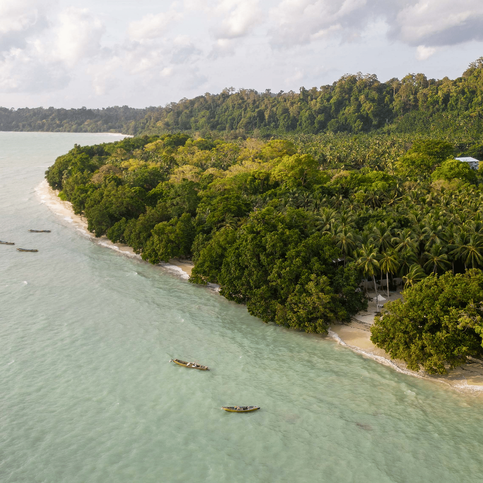 A scenic view of a beach with smooth, sandy shores and clear turquoise waters. The coastline is lined with lush greenery, creating a tranquil and natural setting - Coral Reef Resort & Spa, Havelock