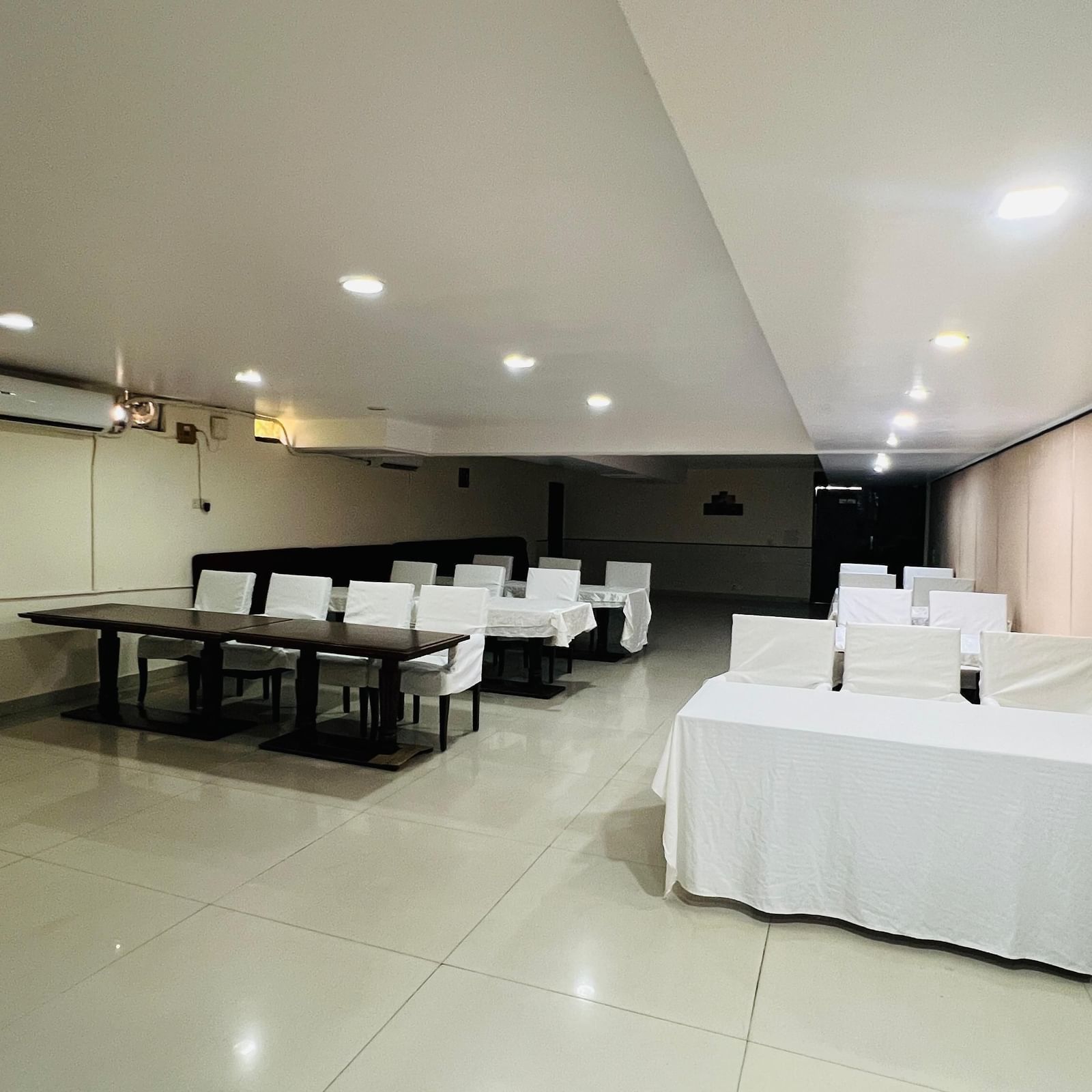  A hotel conference room with long tables and white chairs arranged for an event, featuring modern lighting and light-colored walls. | Hotel Aadhar