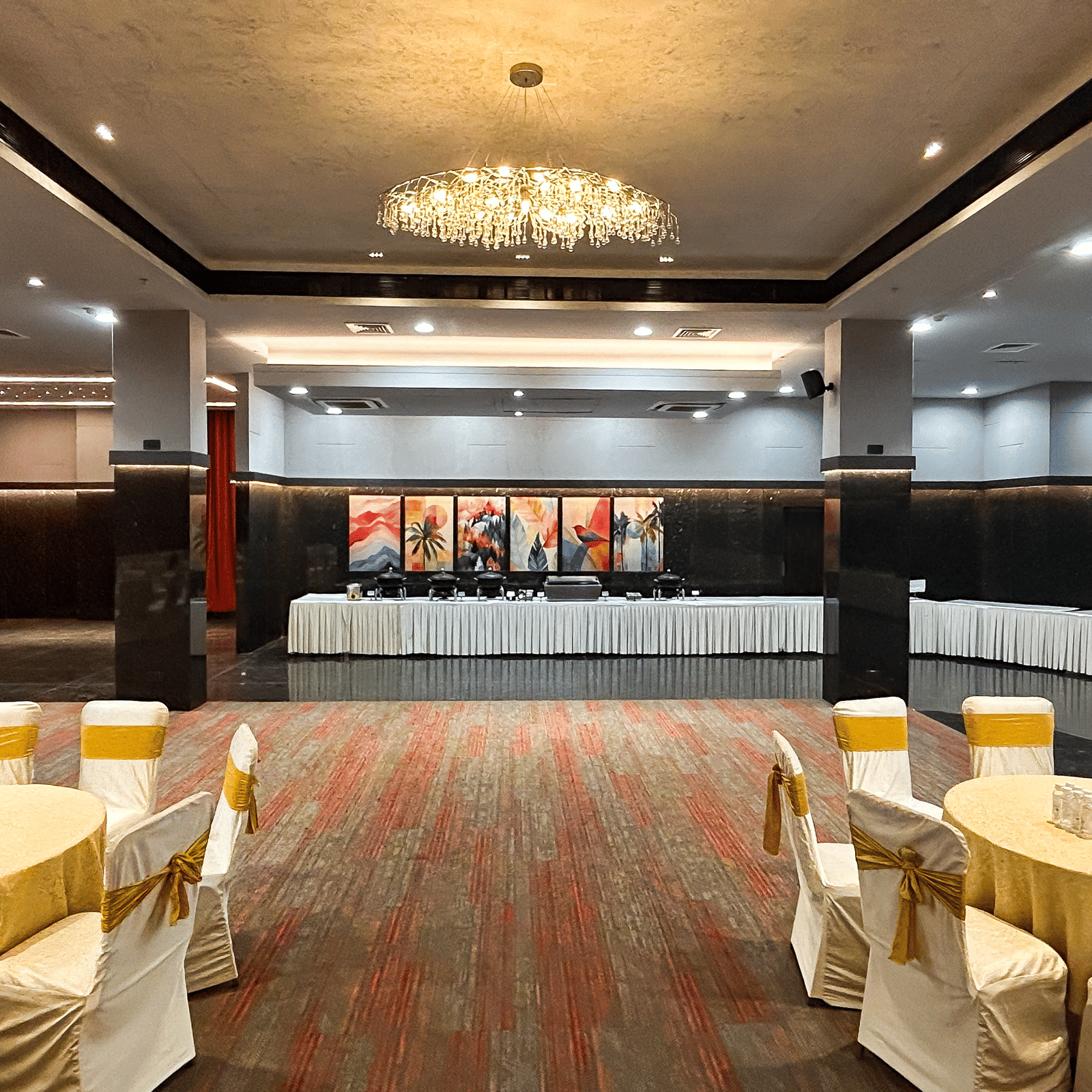 Elegant banquet hall with chandelier, carpet floor, stage, and round tables at Infiniti Hotel, Indore.