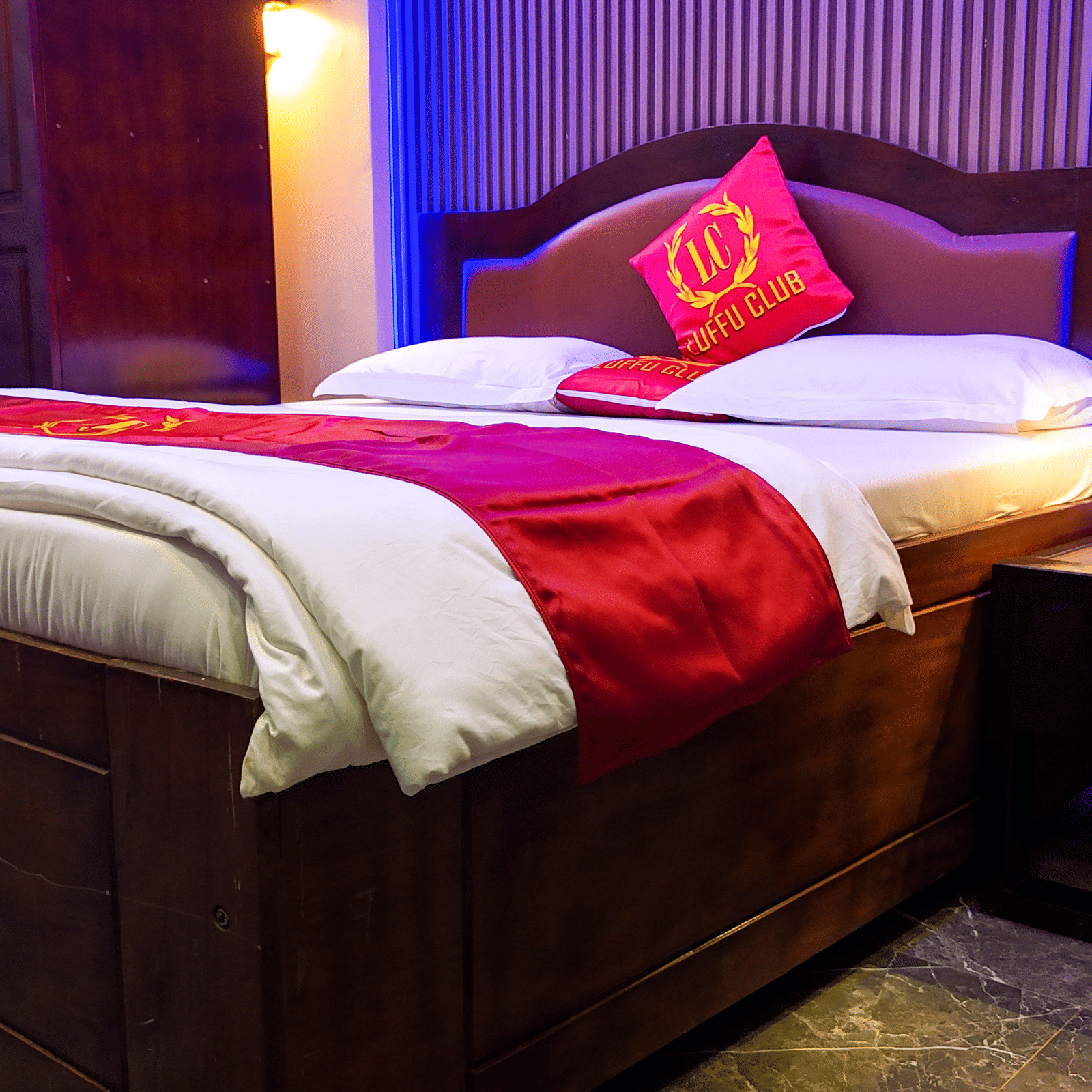 Hotel room with a bed, red bedding accents, and dark wood headboard and side table - Luffu Club