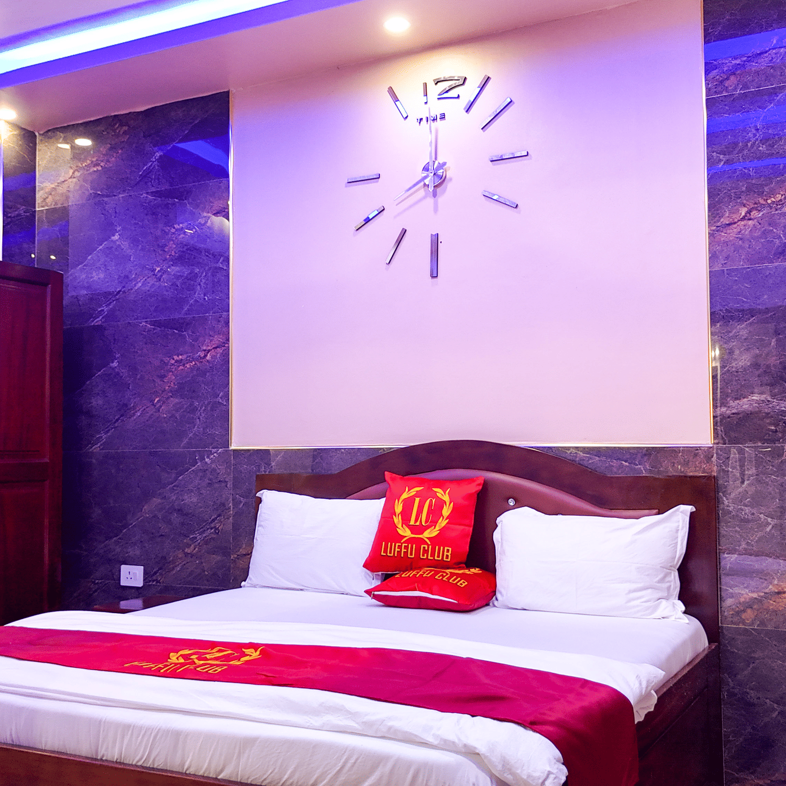 Hotel room interior with a bed, wall clock, wardrobe, and purple lighting - Luffu Club