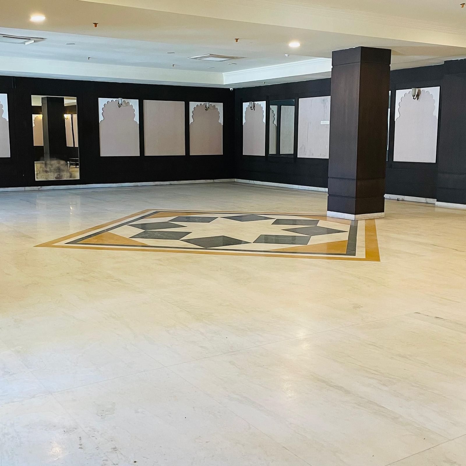 An interior view of Raj Samelan Hall at Shri Vallabh Villas Lords Plaza Nathdwara with a pillar and arranged sofas.