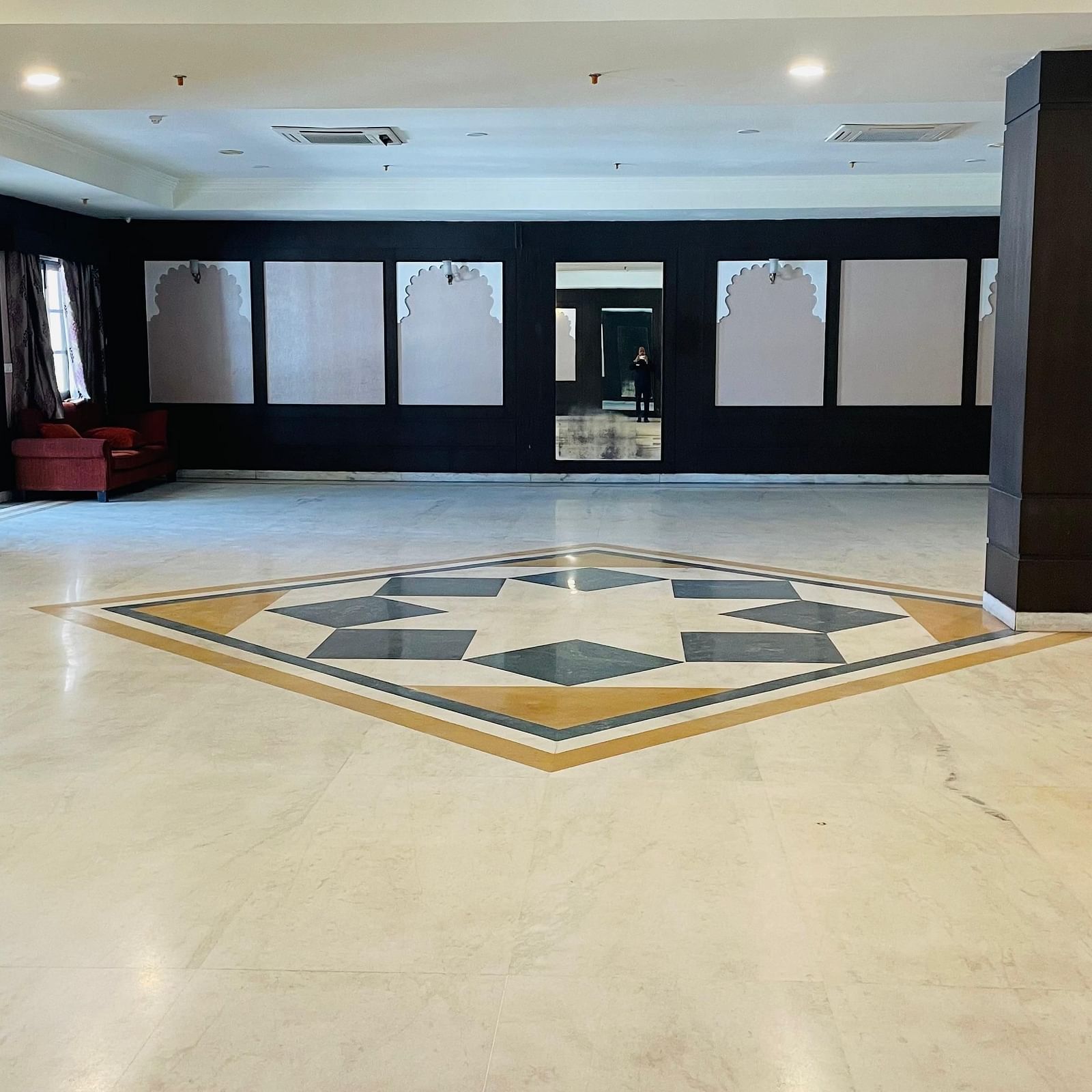 A spacious Raj Samelan hall at Shri Vallabh Villas Lords Plaza Nathdwara with tiled floors, dark columns, and minimal furnishings.