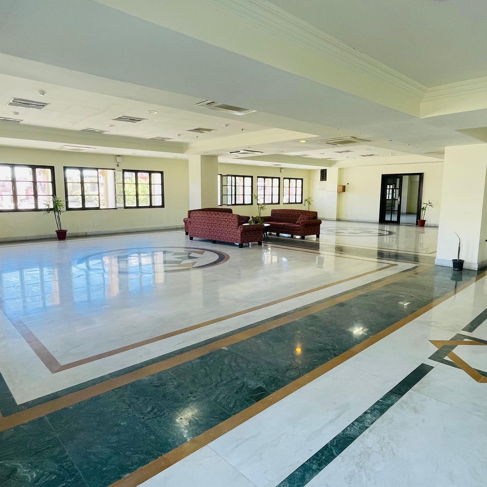 Side wide angle view of Raj Vilas Hall with decorated titled floor, sofas and windows.