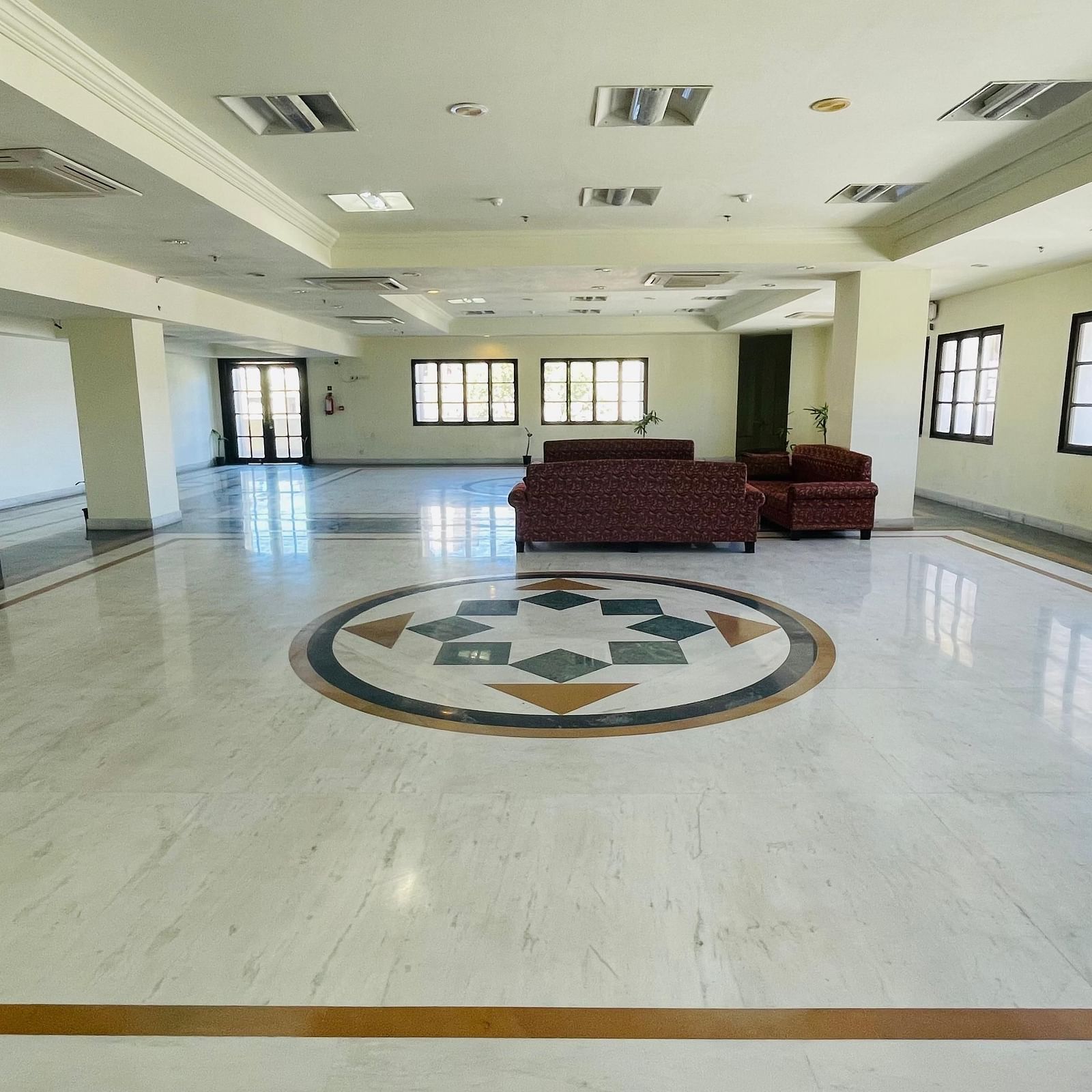 An indoor view of Raj Villas Hall with decorated titled floor, featuring sofas and windows across the room.