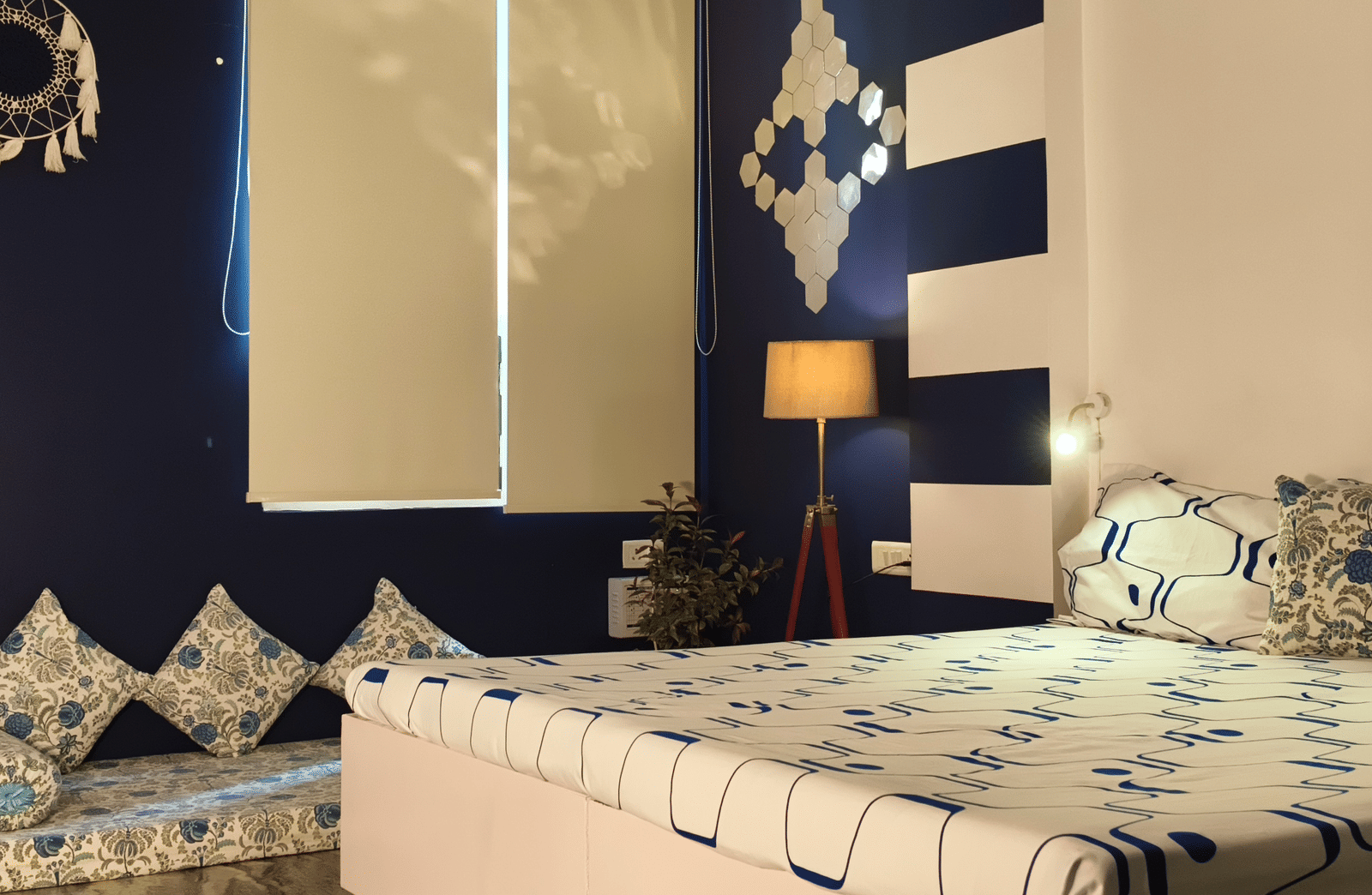 A bedroom with a double bed, patterned bedding, cushions, chairs and a decorative wall backdrop at Jaypore360 Homestay - Best Rooms in Jaipur.