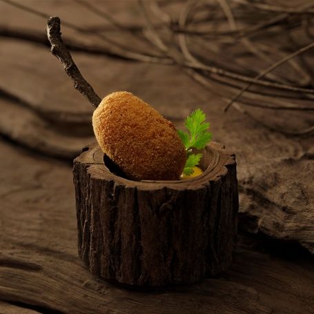 Crispy croquette in a wooden holder with a twig.