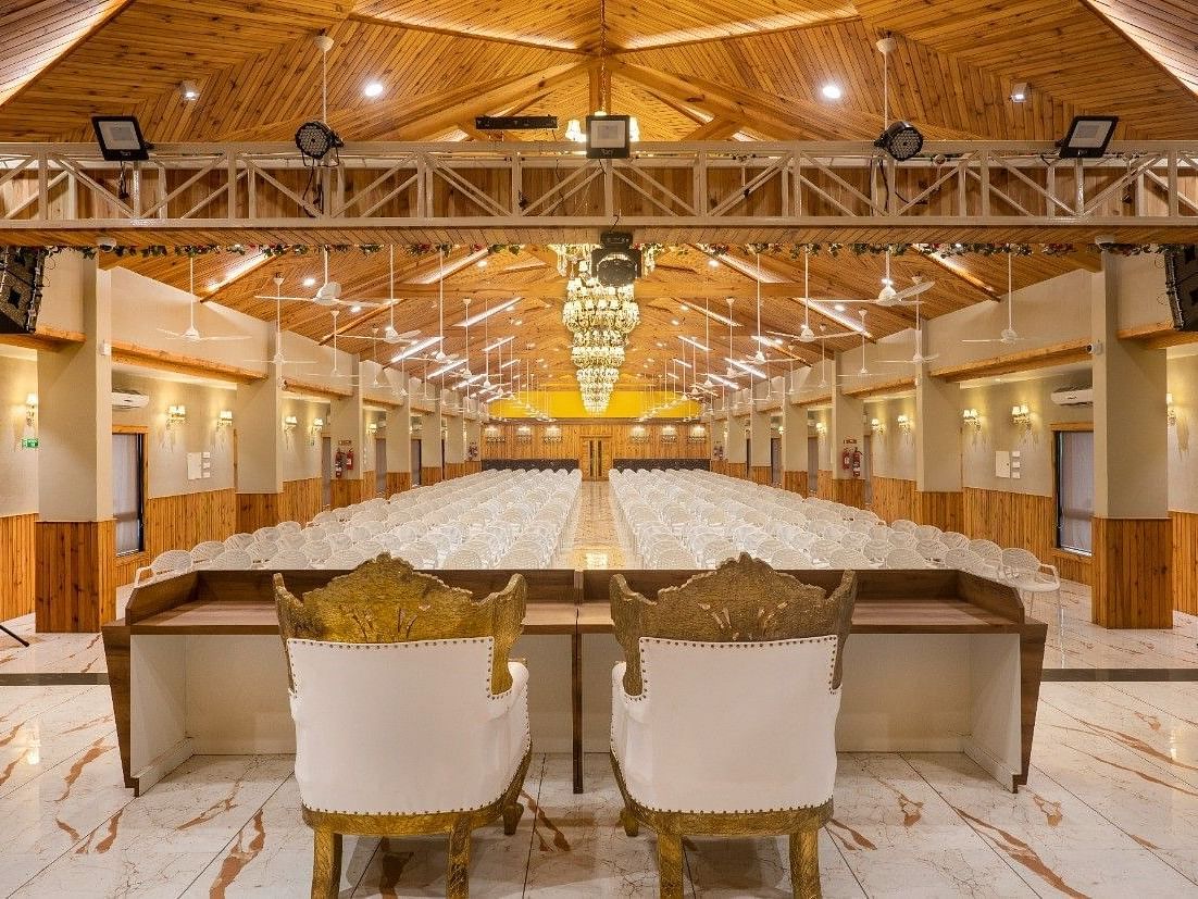 A large banquet hall with a stage area, speakers, and seating at the rear of Angel Lords Eco Inn Amreli.
