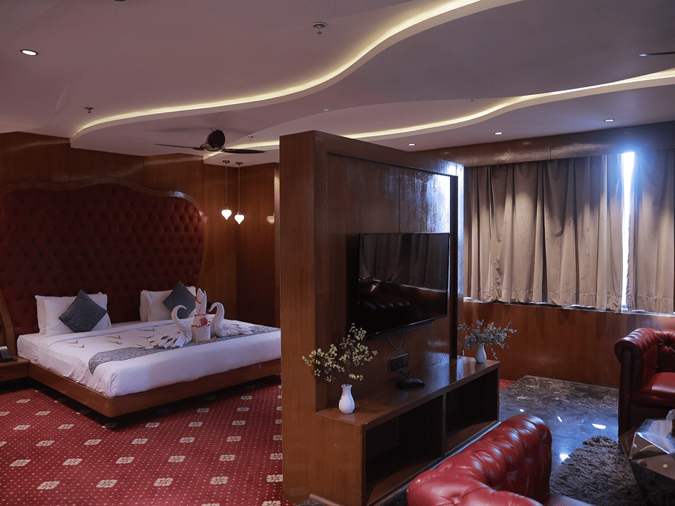 Sky Suite king bed with swan towel art beside a wooden television partition and red leather armchair