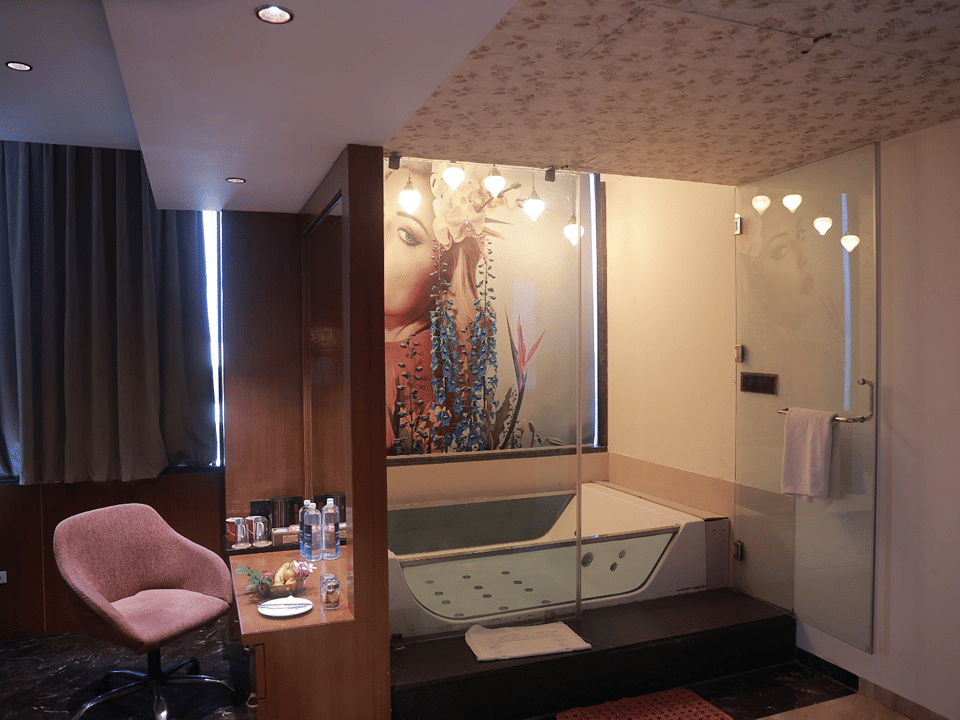 Sky Suite bath with a glass-enclosed Jacuzzi beneath a floral mural and a pink vanity chair